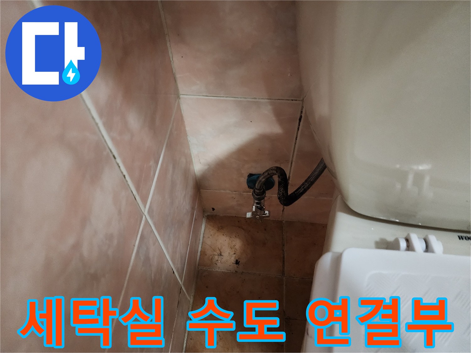 타일 벽면에 고정된 수도꼭지와 검은색 호스의 연결 상태를 촬영한 사진입니다.