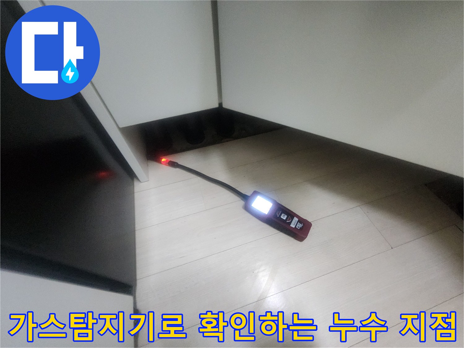 주방 싱크대 하부 공간에서 가스 탐지기를 사용하여 배관의 이상 여부를 점검하고 있습니다.