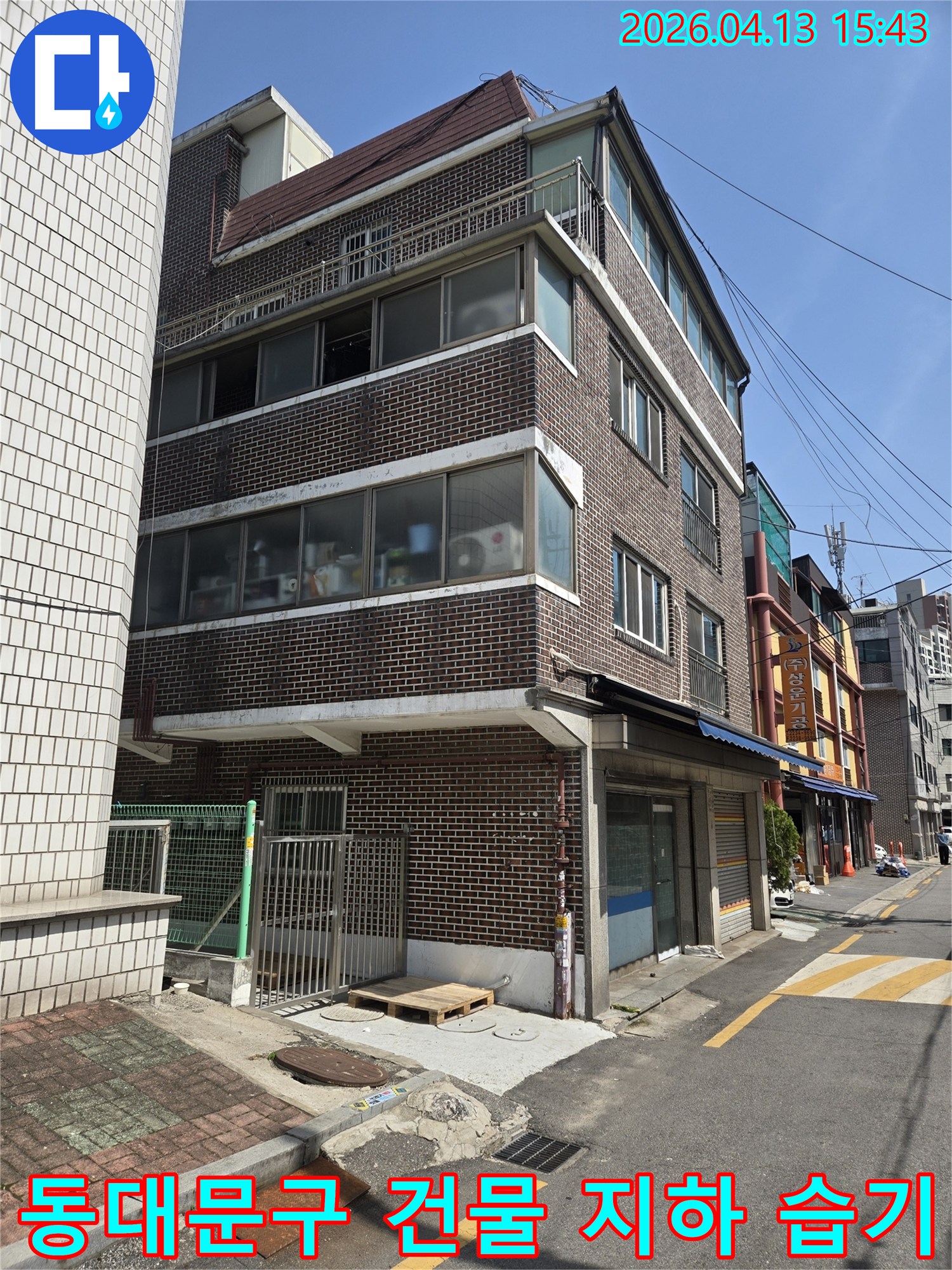 동대문구의-건물-외관을-보여주는-이-사진은-지하층-습기-및-곰팡이-문제로-인한-누수-원인을-찾기-위해-전문-엔지니어가-현장을-점검하는-모습입니다.