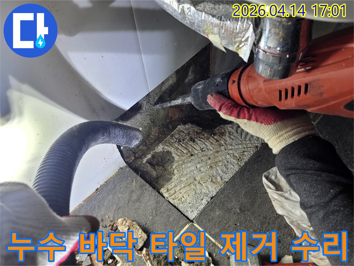 누수 탐지 후 바닥 타일을 제거하는 작업자가 드릴을 사용하며-파손된 타일과 진공 호스가 함께 보이는 누수 공사 현장