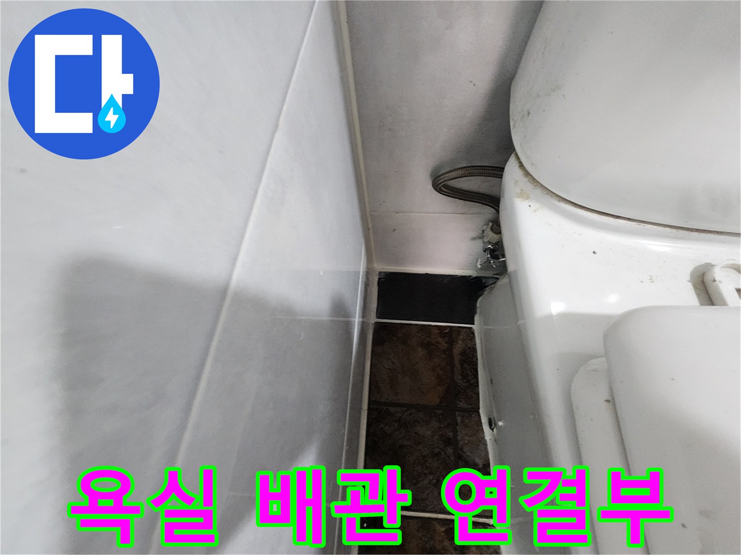하얀색 변기 옆으로 지나가는 은색 배관과 벽면 타일