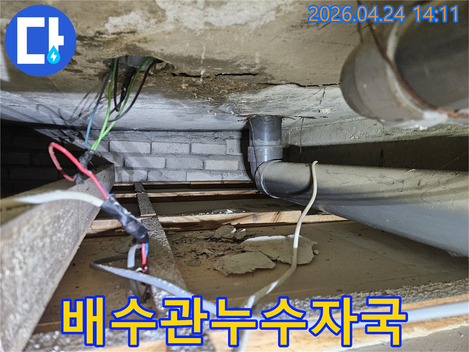 콘크리트 천장 아래-배수관 주변에 생긴-오래된 누수 자국과-손상된 전기선을 보여주는 이미지입니다