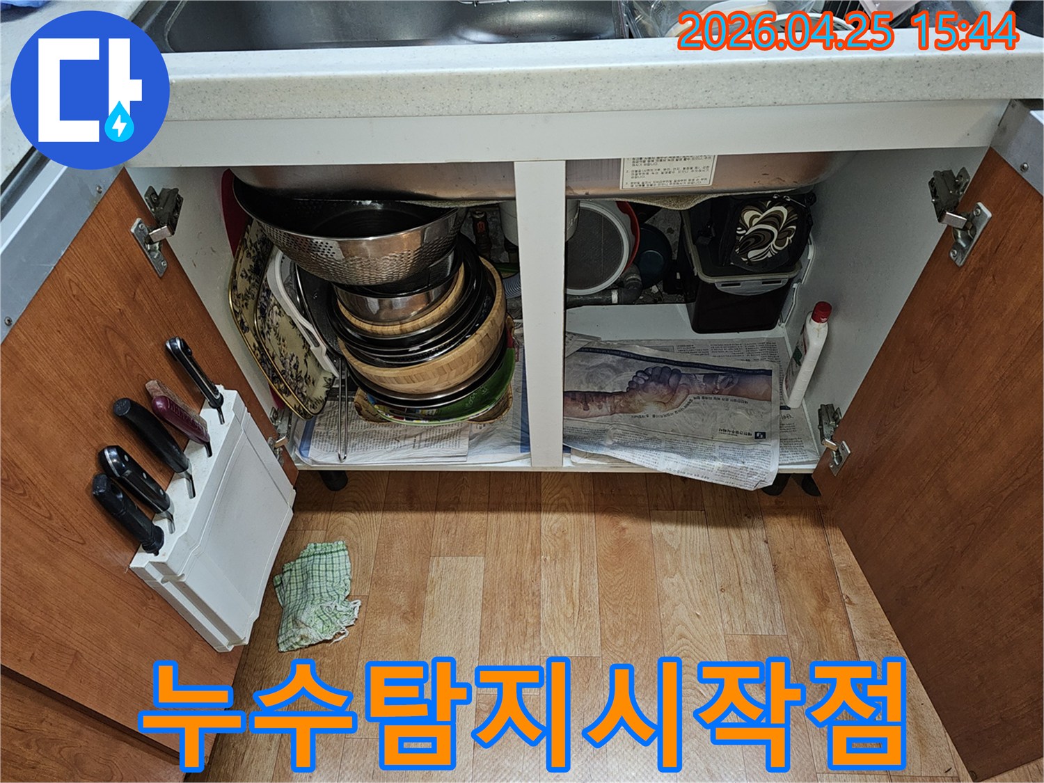 싱크대 하부장 내부 모습-누수 점검을 위해-그릇과 배관이 보이고 바닥에 신문지가 깔려 있습니다.