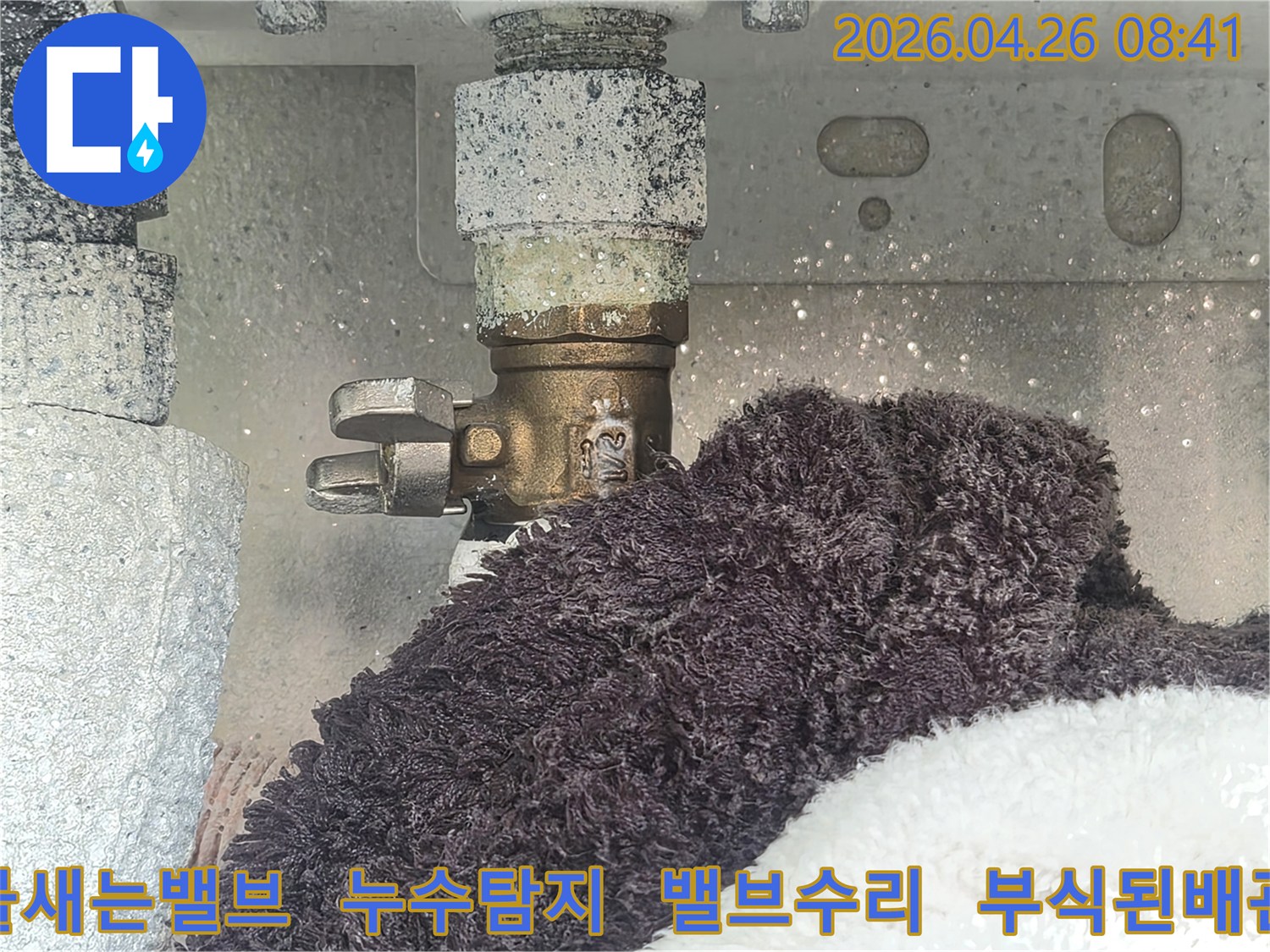부식으로 인해 하얗게 변색된 수도 밸브에서 물이 새고 있는 현장-아래 수건이 젖어있는 모습-누수 문제의 시급성을 보여주는 이미지