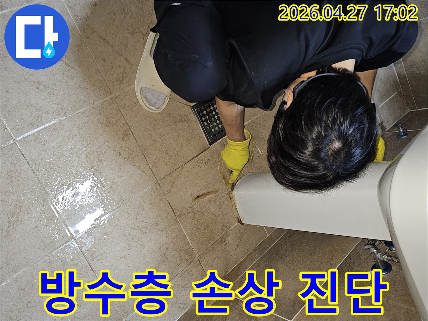 전문 엔지니어가-노란 장갑을 끼고-욕실 바닥의 젖은 타일과-세면대 하단부를-집중적으로 관찰하며-방수층 손상 가능성을 진단합니다