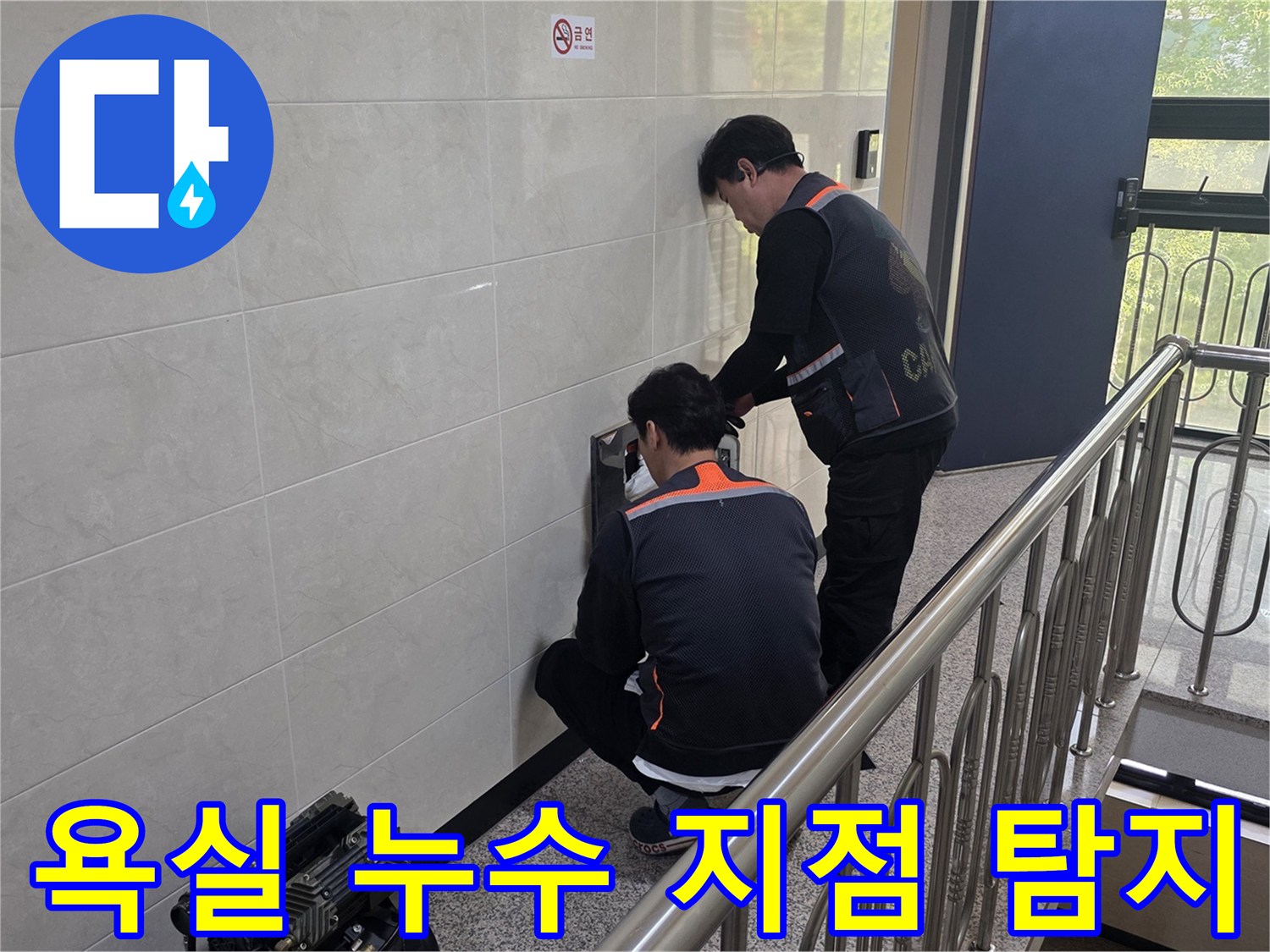 두 명의 전문 기술자가 건물 벽면의 욕실 누수 의심 지점을 정밀하게 탐지하고 있습니다-정확한 원인 파악을 통해 쾌적한 욕실 환경을 되찾기 위한 작업입니다.