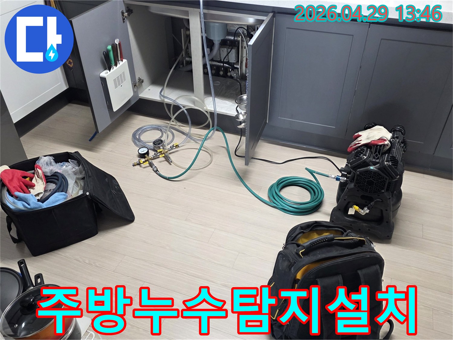 동안구 주방 싱크대 하부에서-누수 탐지를 위한-압력 게이지와 호스-그리고 공기 압축 장비를-설치하는 작업이 진행 중입니다