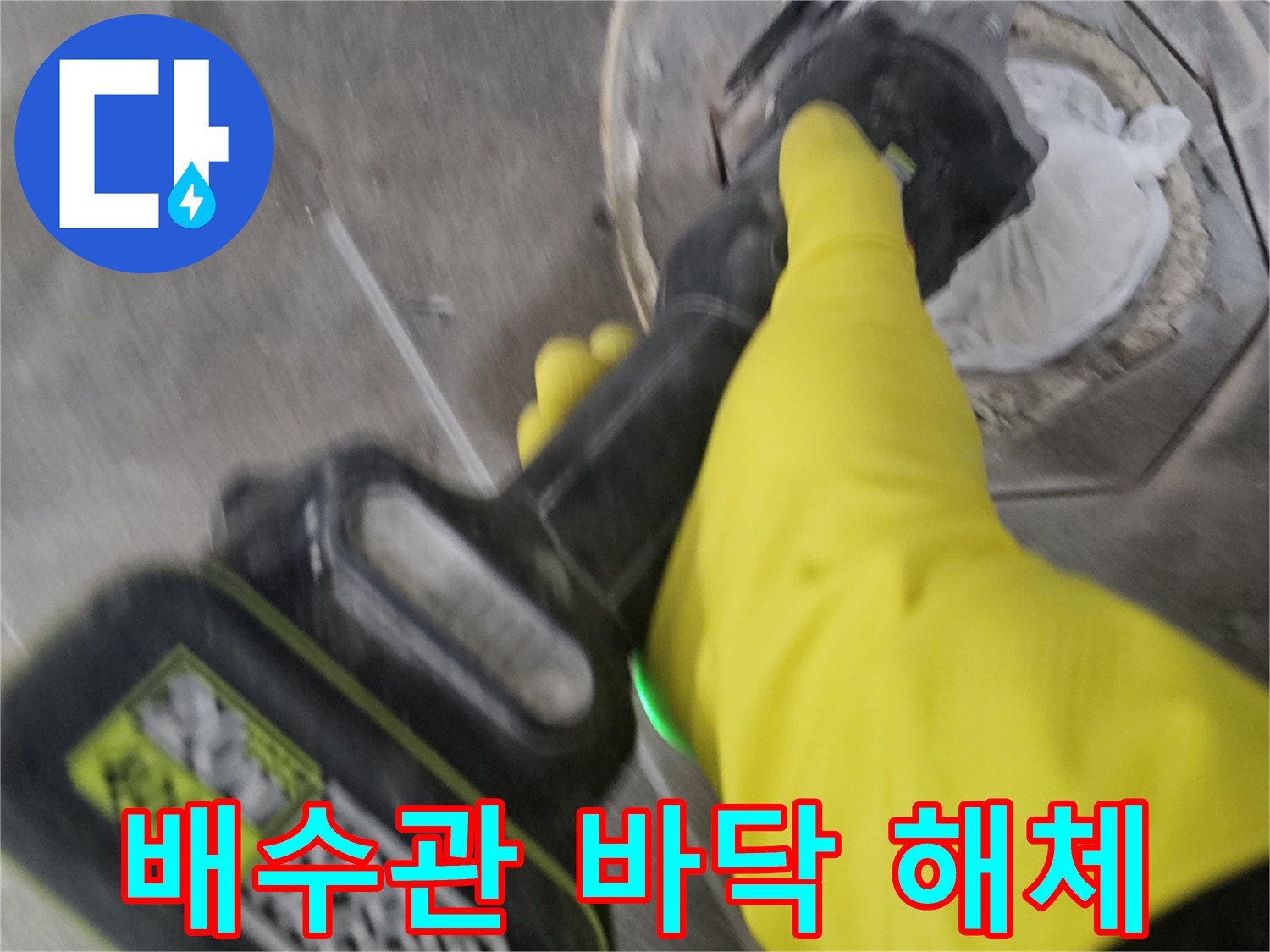노란색 안전 장갑을 착용한-기술자가-전동 공구를 사용하여-배수관 주변의 바닥 타일을-정교하게 해체하는 현장입니다.