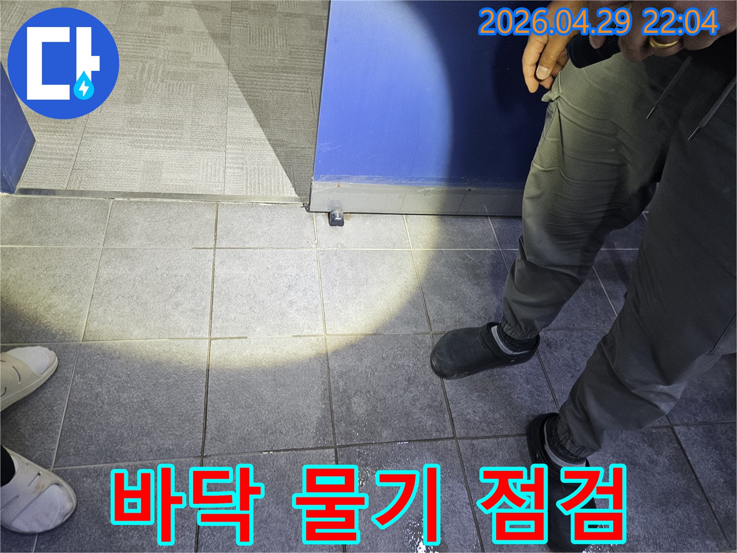 누수 탐지 전문가가 바닥에 고인 물기를 보고-누수 발생 여부와 대략적인 위치를 파악하고 있습니다.