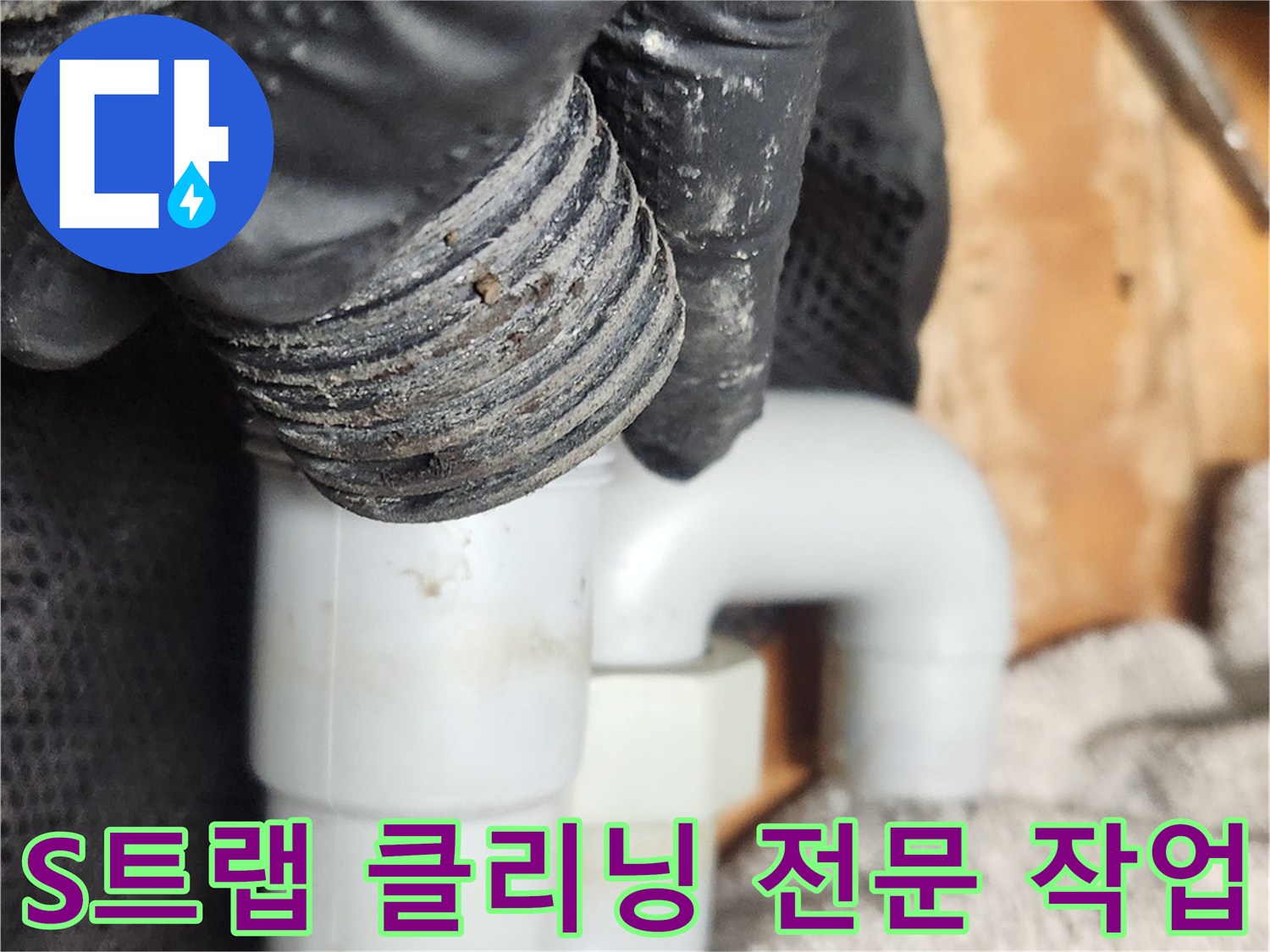 검은 장갑을 낀 손이-오염된 S트랩 배관을 분리하여-전문적인 클리닝을 준비하는 모습입니다