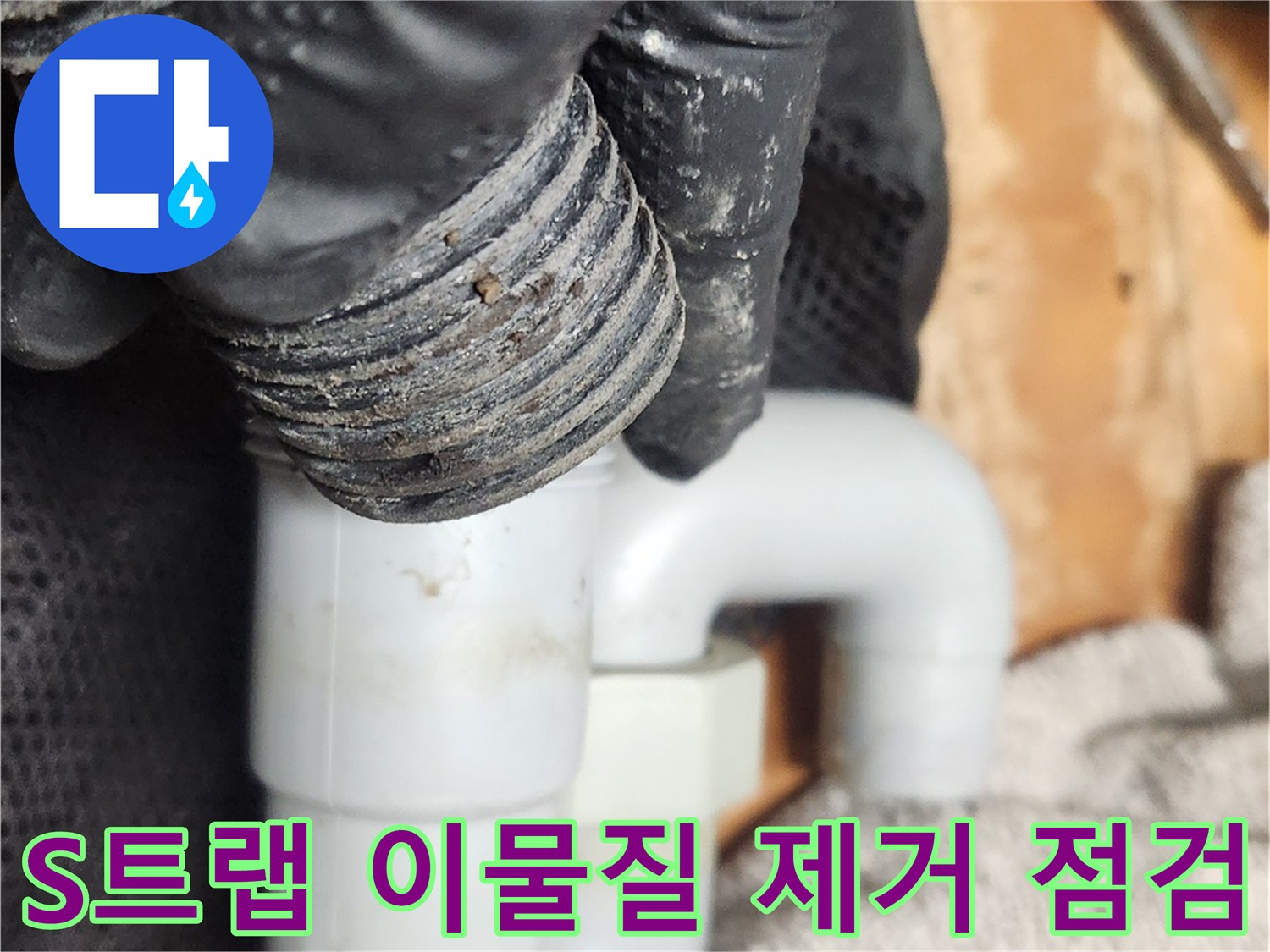 작업자가 검은 장갑을 끼고-오염된 S트랩 배관을 분리하여-내부 이물질을 제거하고 배관 상태를 점검하고 있습니다