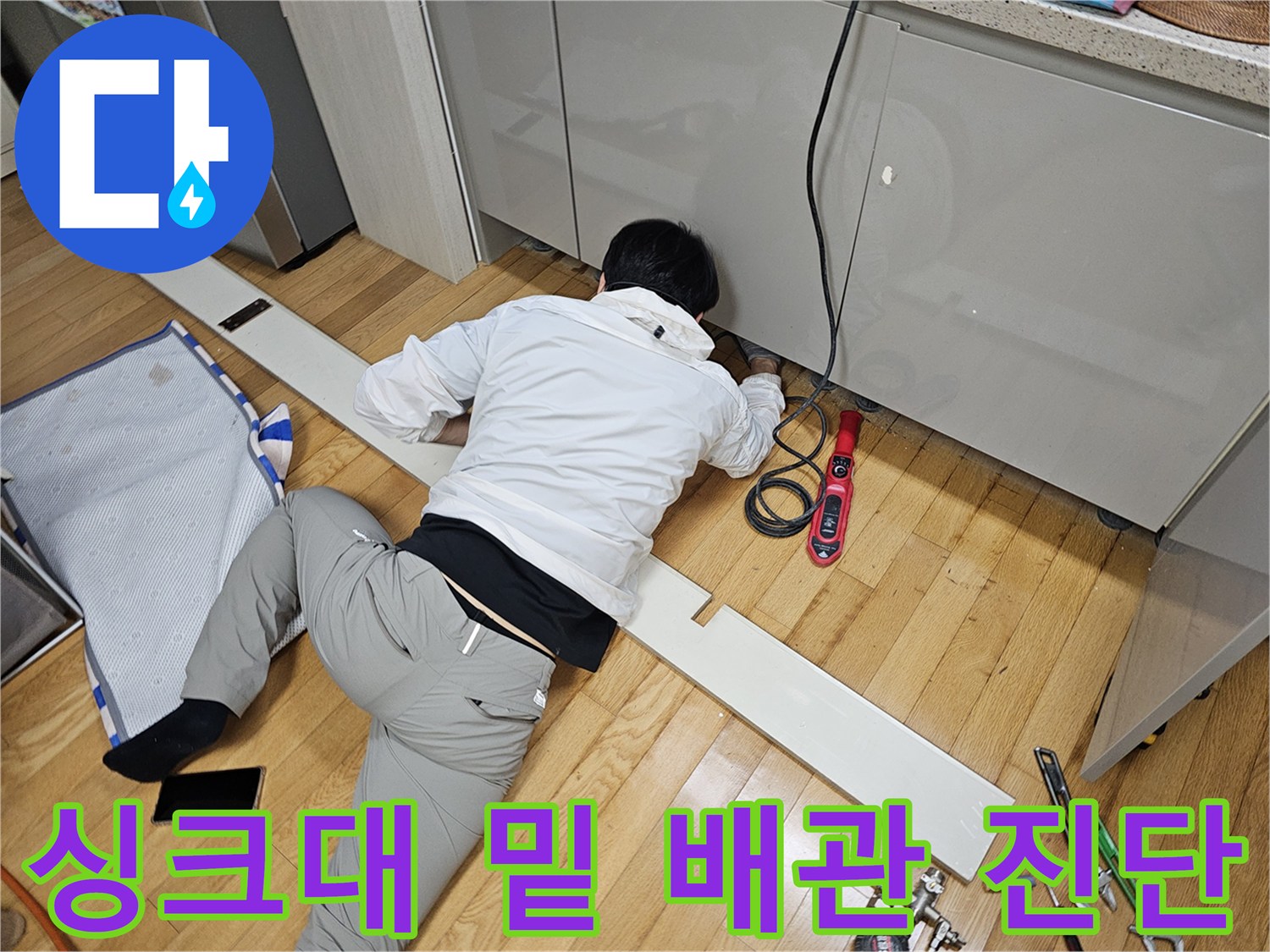 주방 싱크대 하부 공간에서 배관 누수 지점을 찾는 작업 현장