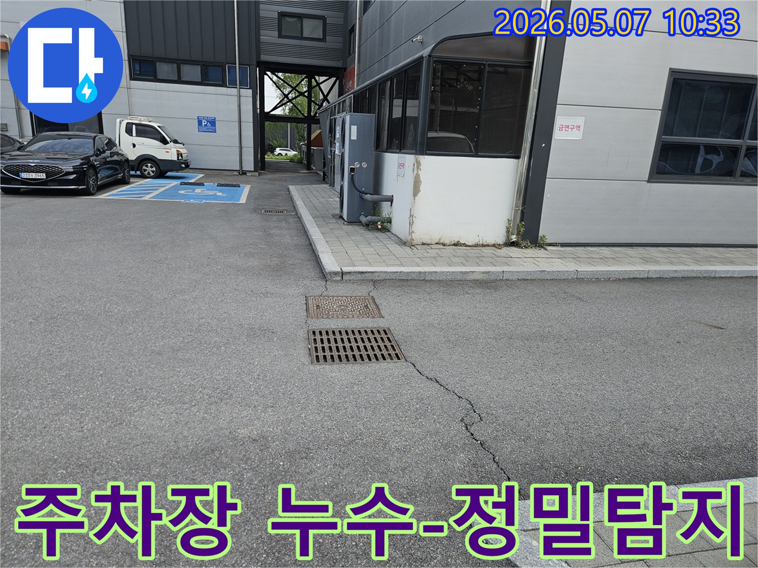 이 이미지는 의정부시 만가대길 주차장의 아스팔트 균열과-맨홀-배수구 주변의 지반 침하 징후를 보여주며-정밀 누수 탐지가 필요한 현장입니다.