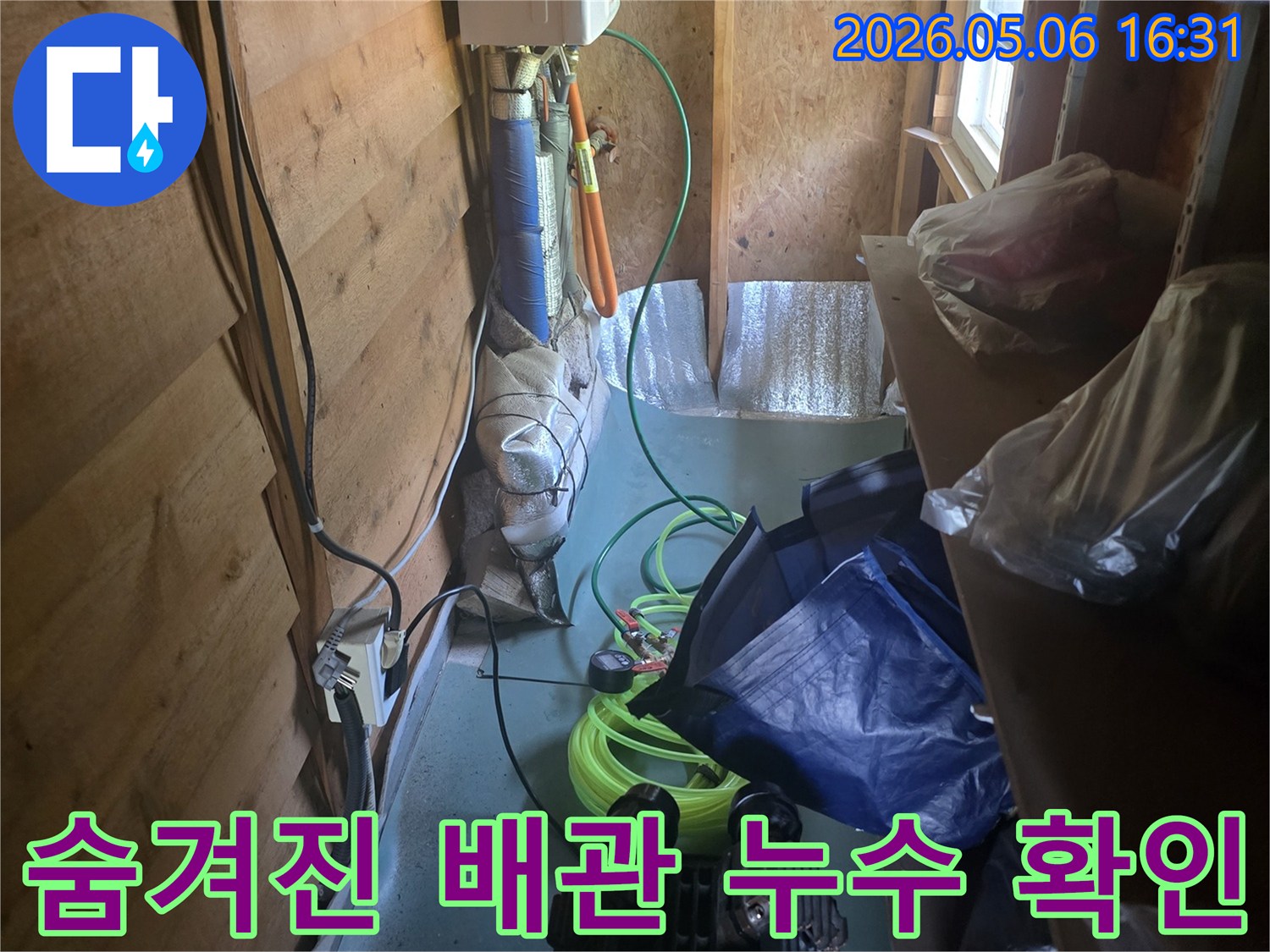 물건들이 쌓인-좁은 틈새에서-누수 발생 지점을-정확히 파악하려는-전문가의 세심한 작업