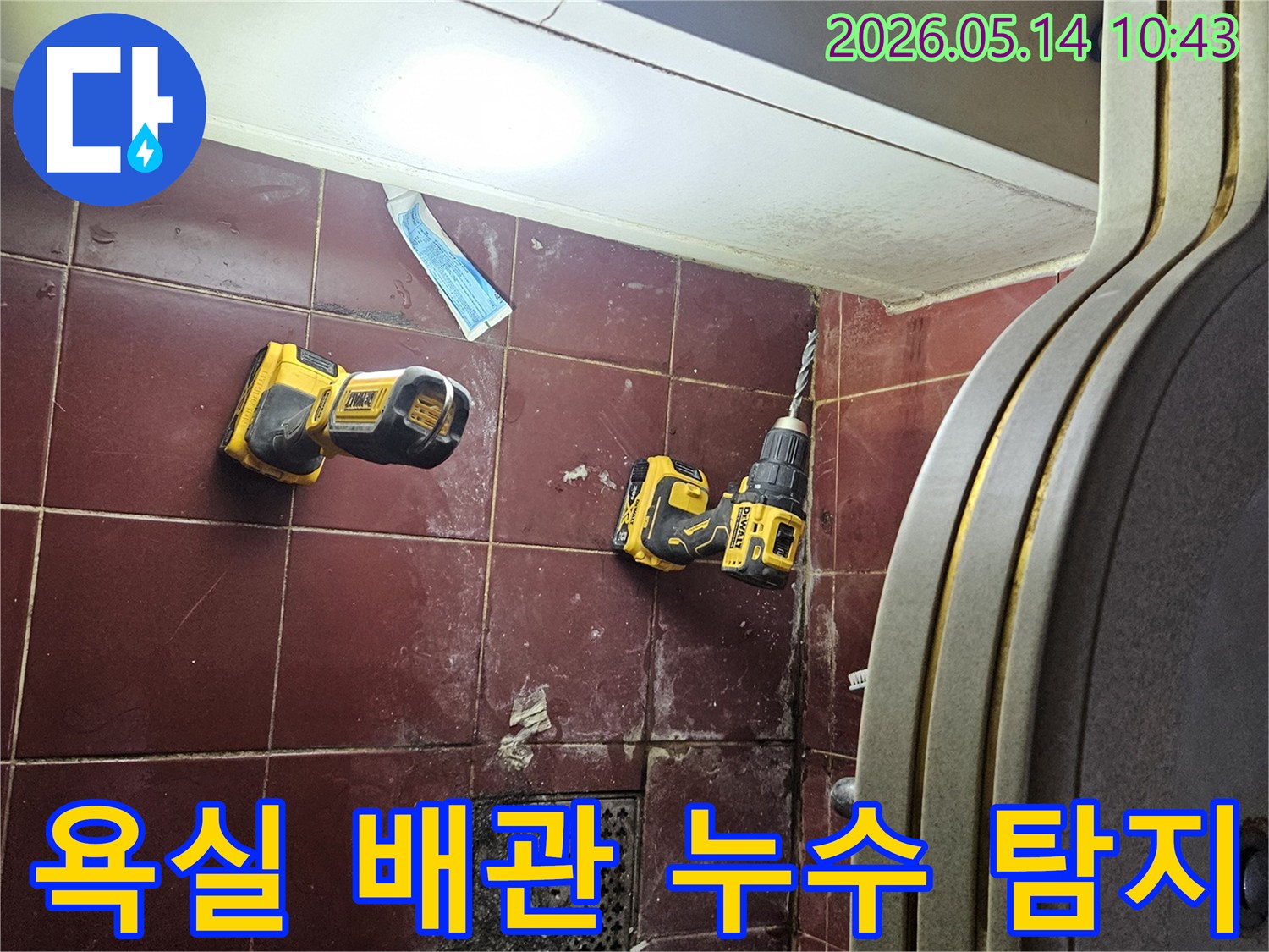 붉은 타일 바닥에 놓인 전동 드릴과 작업용 손전등-욕실 배관 누수 탐지를 위한 장비들입니다