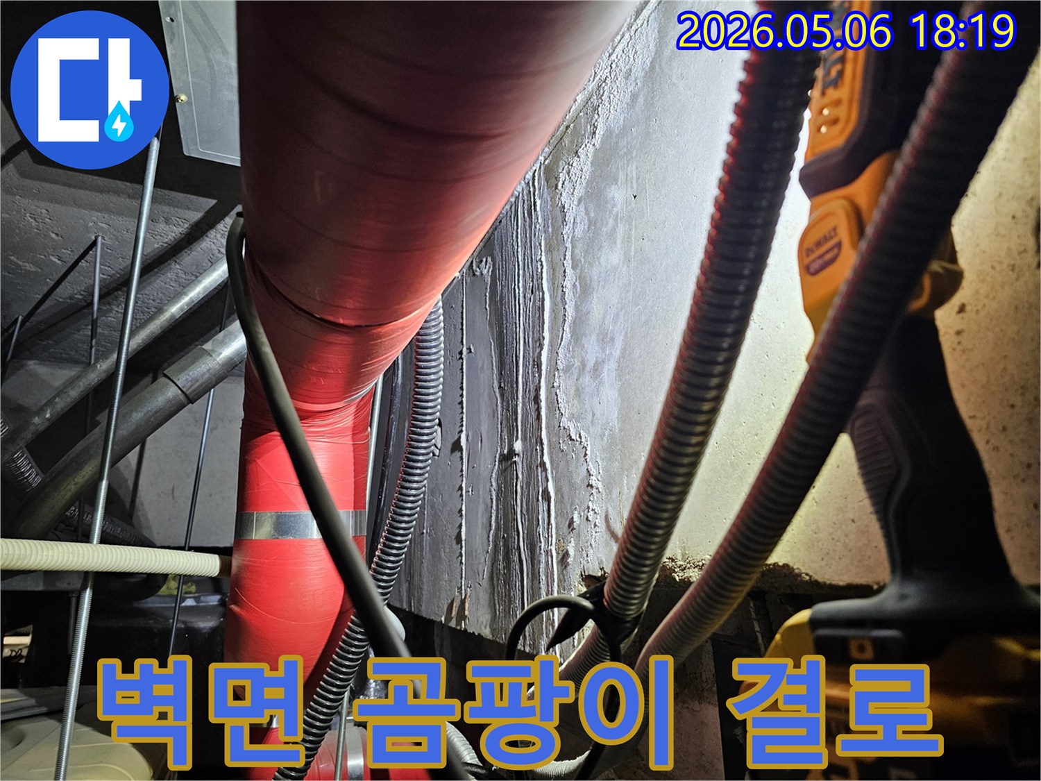 어두운 지하 공간의-빨간색 배관 옆-벽면에-나타난-습기와-물자국을-통해-곰팡이 및-결로 현상을-진단하는-모습