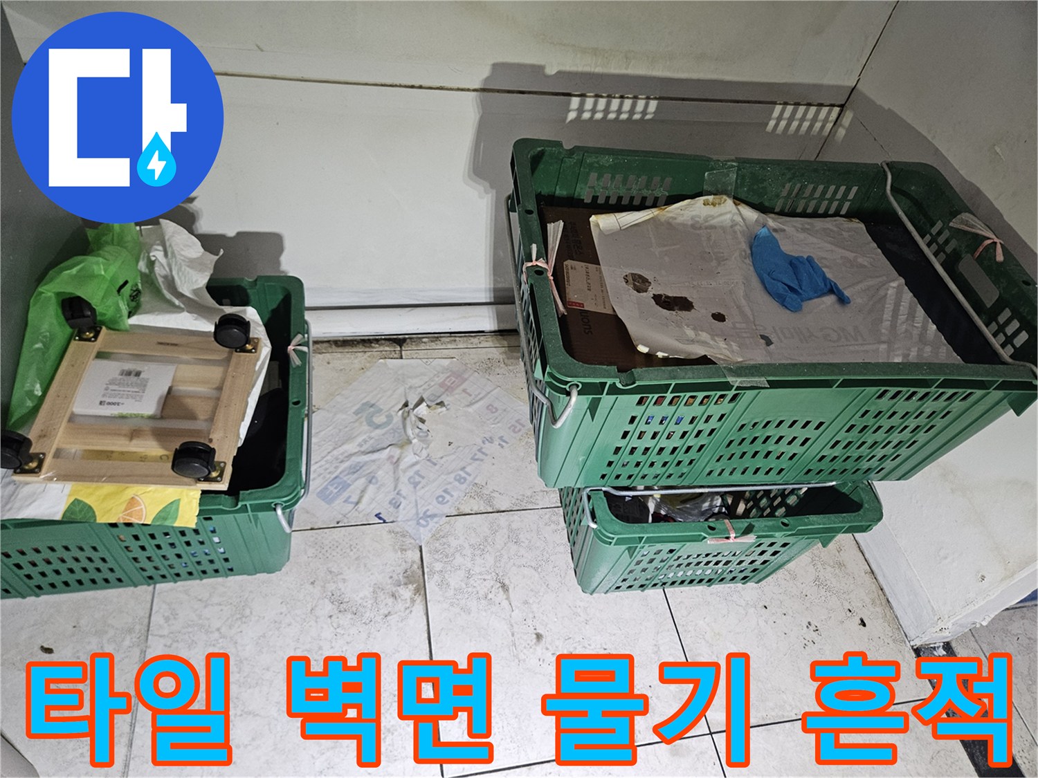 타일로 마감된-벽면 하단에-누수로 인한-습기와-오염 흔적이-보이는-현장 사진으로-물건들이-주변에-놓여있습니다