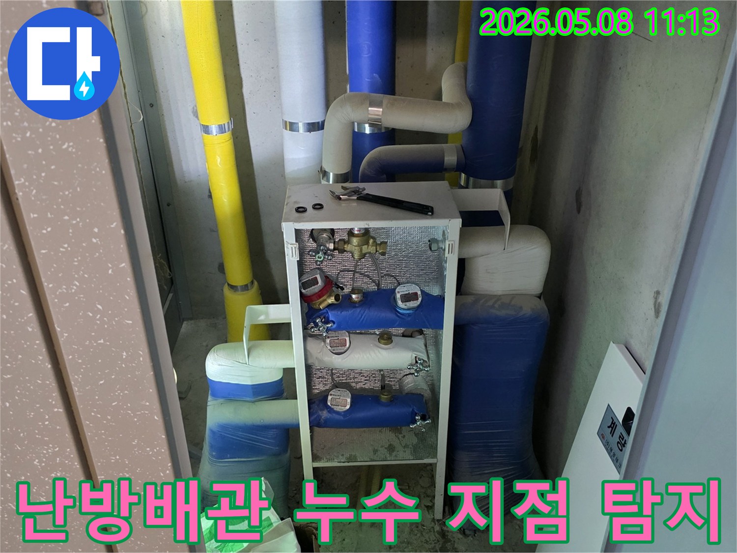 이 이미지는 건물의 난방 시스템과 관련된-다양한 색상의 단열재로 감싸진 배관과-수도 계량기-그리고 작업 도구를 보여주며-난방 배관 누수 점검의 중요성을 강조합니다