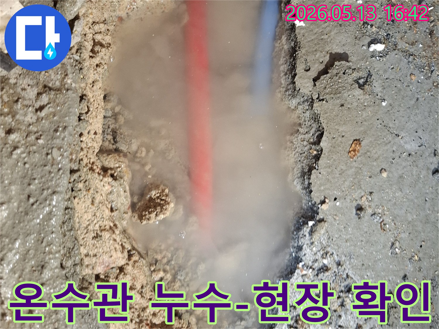 흙탕물 속에서-붉은색과 푸른색 배관이-보이는 누수 현장으로-수증기가 활발하게 뿜어져 나오는-긴급한 상황을 보여줍니다