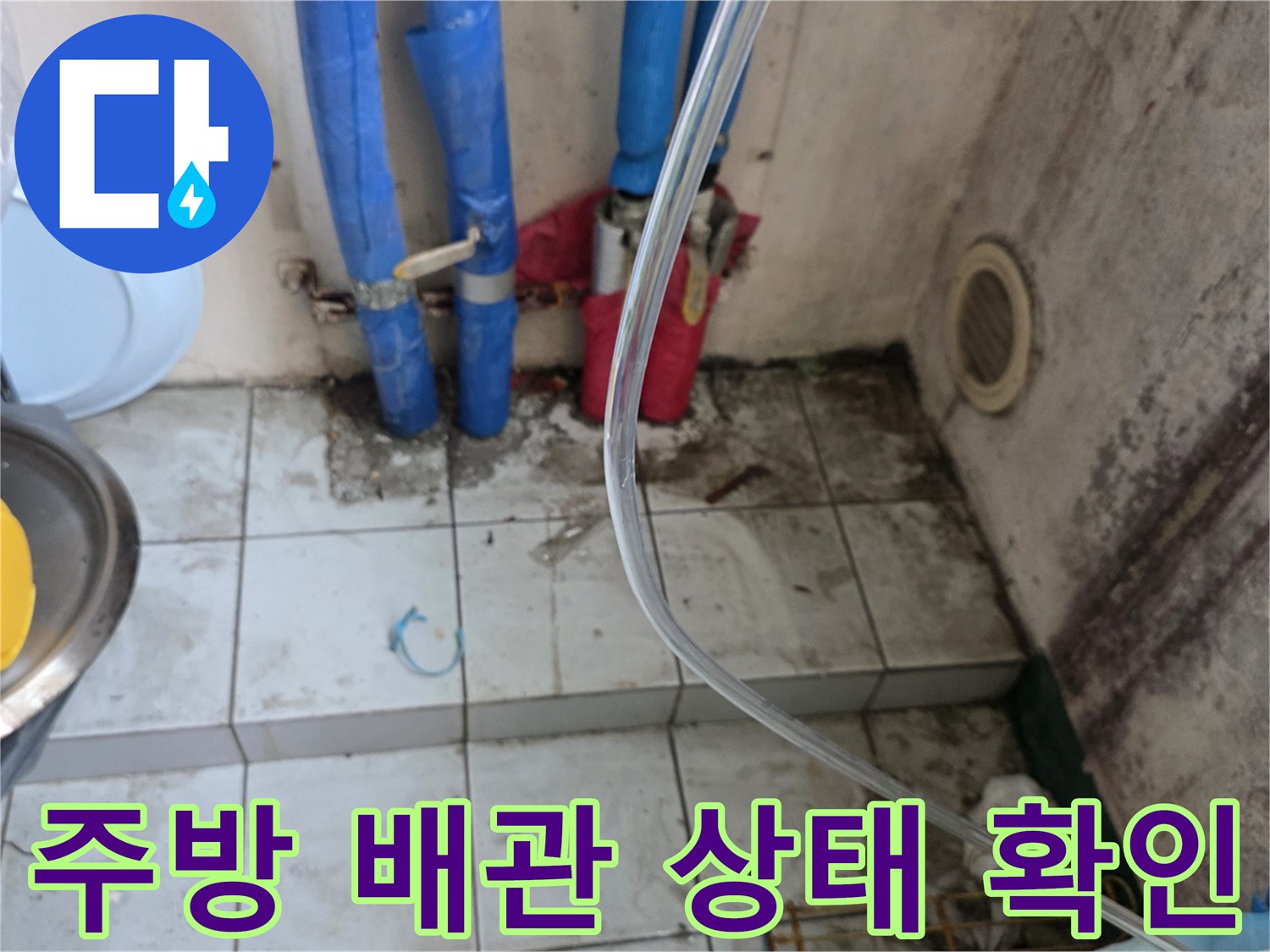싱크대 하부장 근처의 파란색 배관과 타일 바닥 모습입니다.
