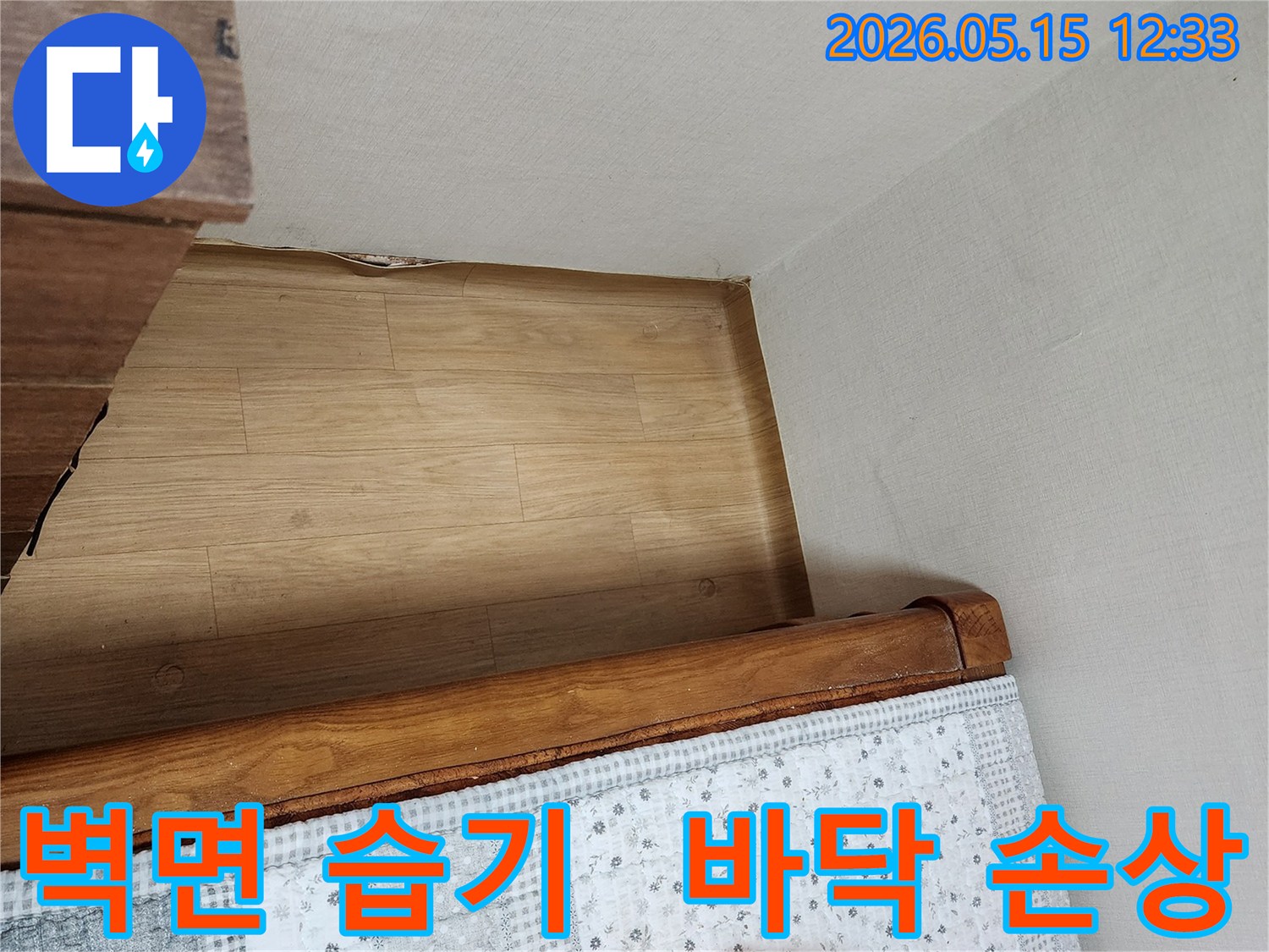 침대-옆-벽면의-습기-자국과-바닥-마루의-손상-징후를-보여주는-누수-현장-사진입니다