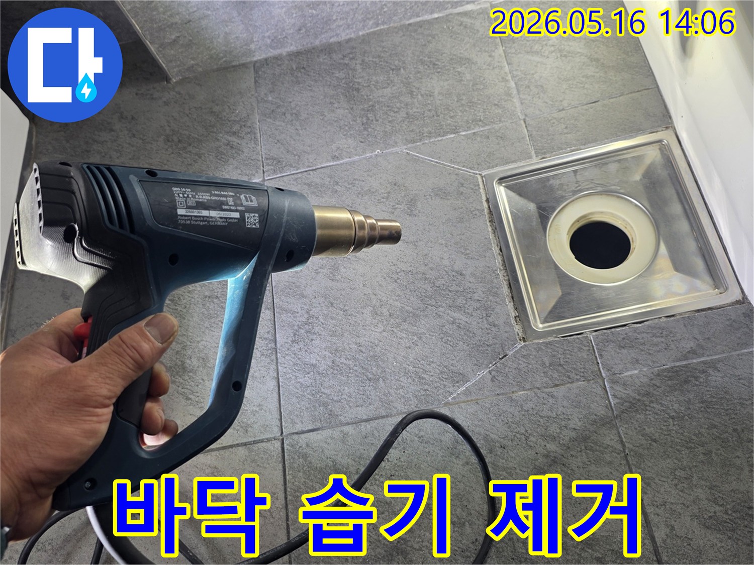 누수 전문가가 욕실 바닥의 배수구 주변을 열풍기로 건조하여-누수 탐지 전 습기를 제거하는-모습입니다.