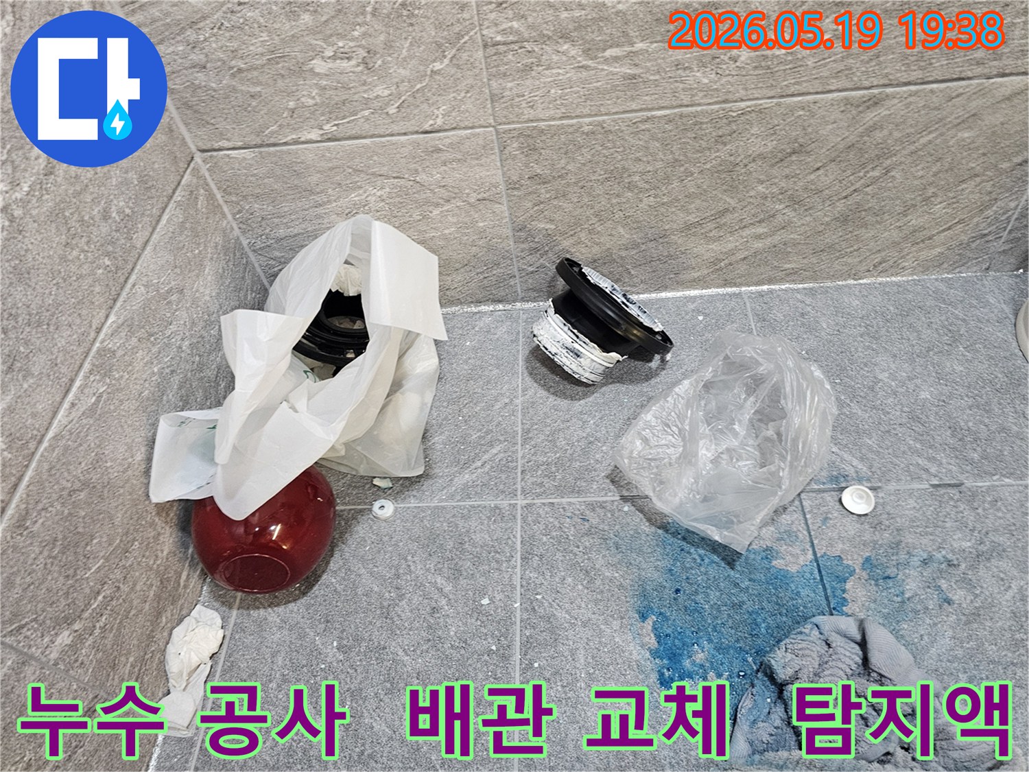 누수 공사 현장에서-파란색 탐지액으로 확인된 누수 지점과-교체된 배관 부품들이 바닥에 놓여 있습니다