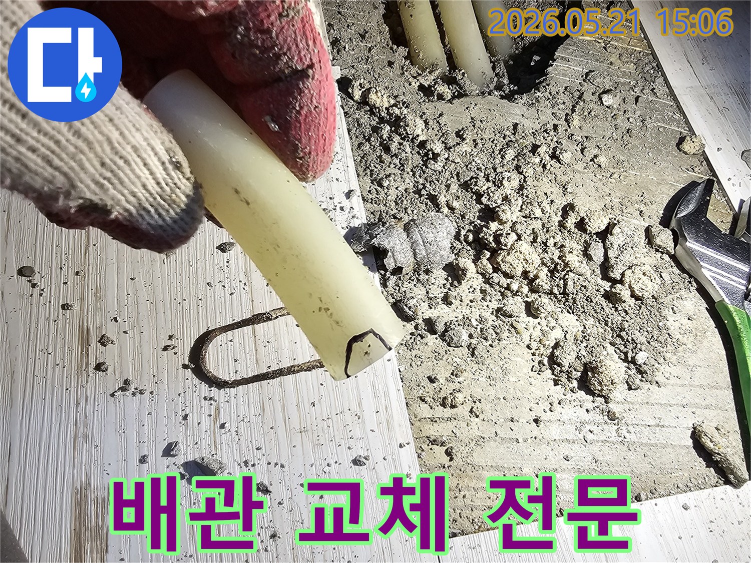 작업 장갑을 낀 손이 파손된 배관 조각을 들고-전문적인 교체 공사를 설명하는-현장 사진입니다