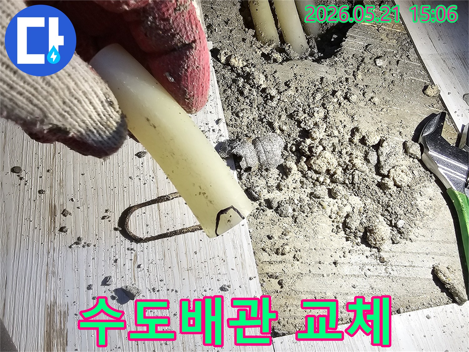 작업 장갑을 낀 손이 파손된 수도배관 조각을 들고-교체 작업을 설명하는-현장 사진입니다