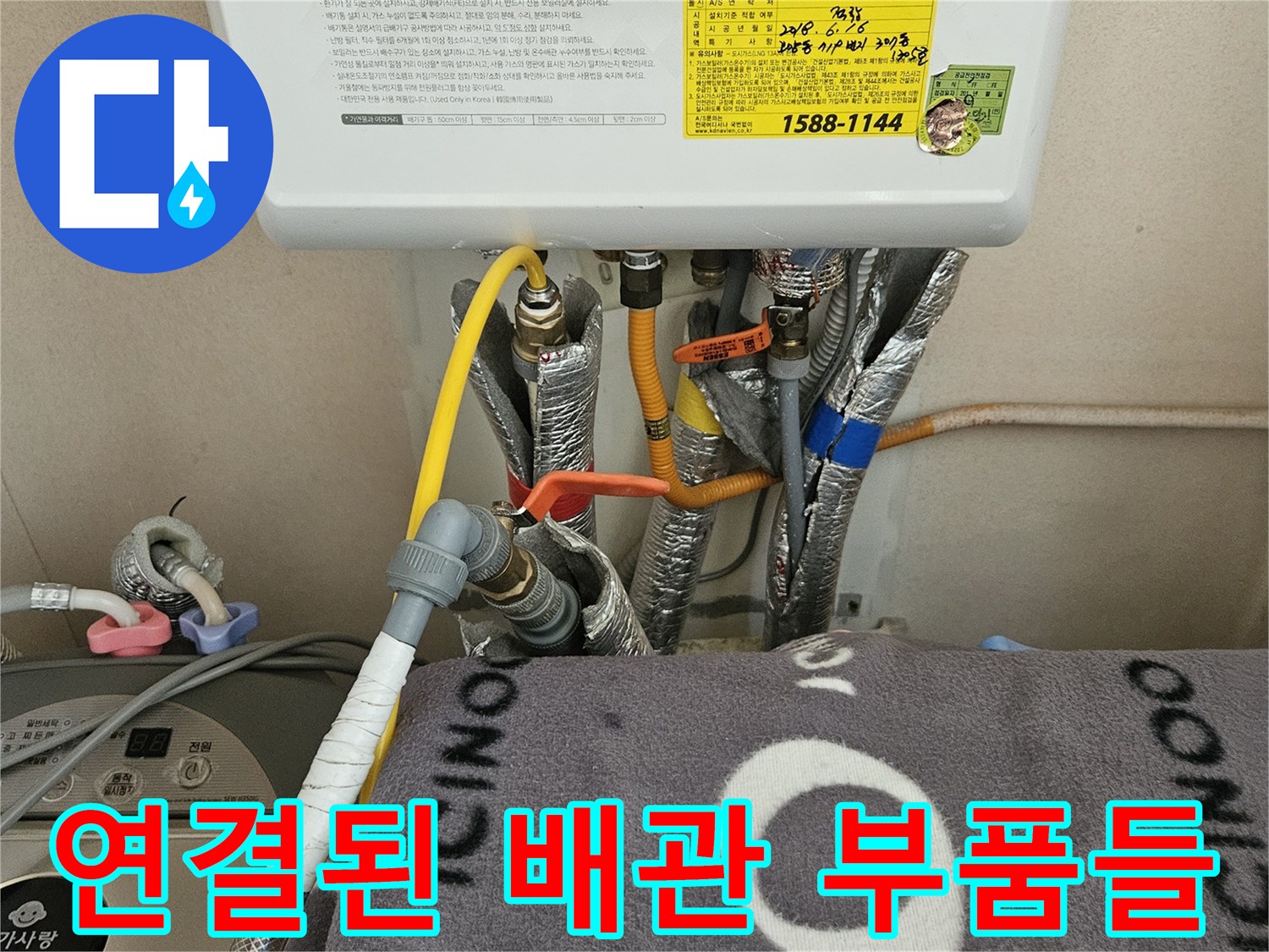 보일러 하단에 복잡하게 연결된 유연한 호스와 금속 배관의 모습