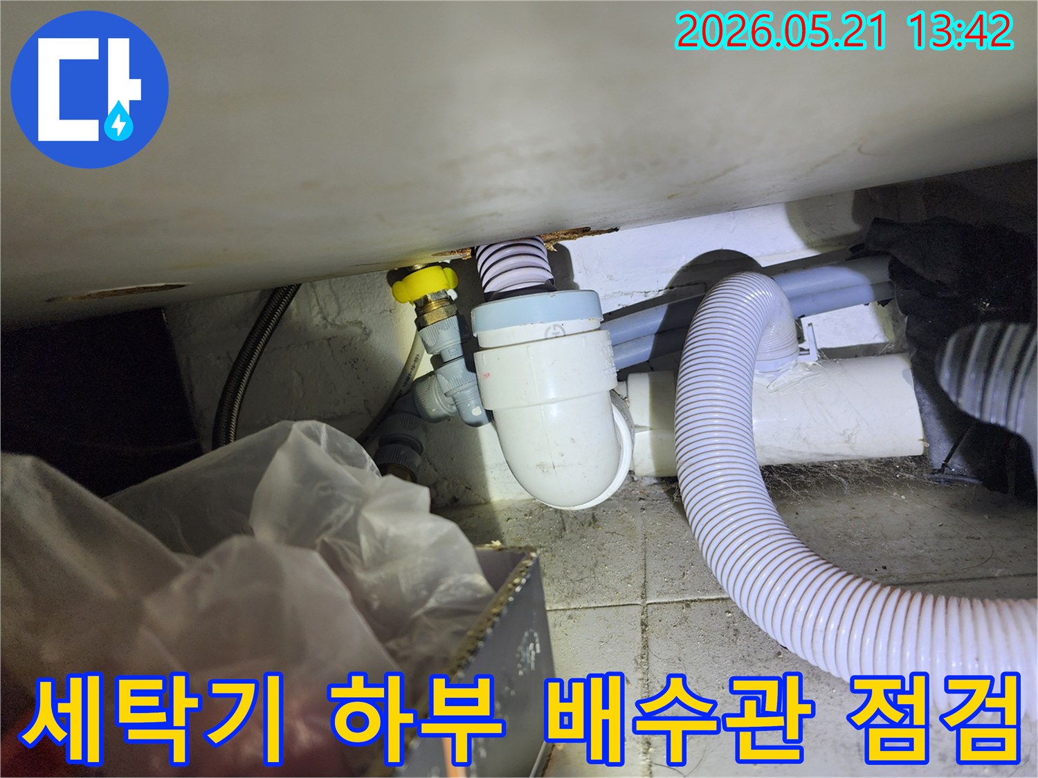 세탁기 하부에서 발생하는 누수 지점을 확인하기 위해-배수관 연결 부위를 정밀하게 점검하는 모습입니다.