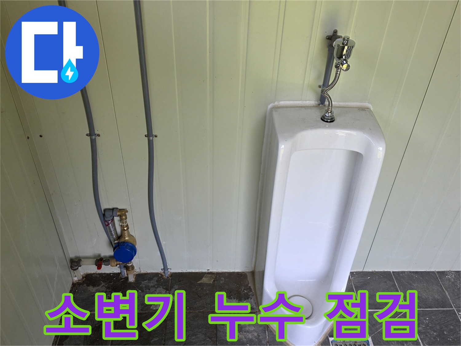 소변기 옆 벽면에 설치된 파란색 계량기와 급수 배관의 모습입니다.