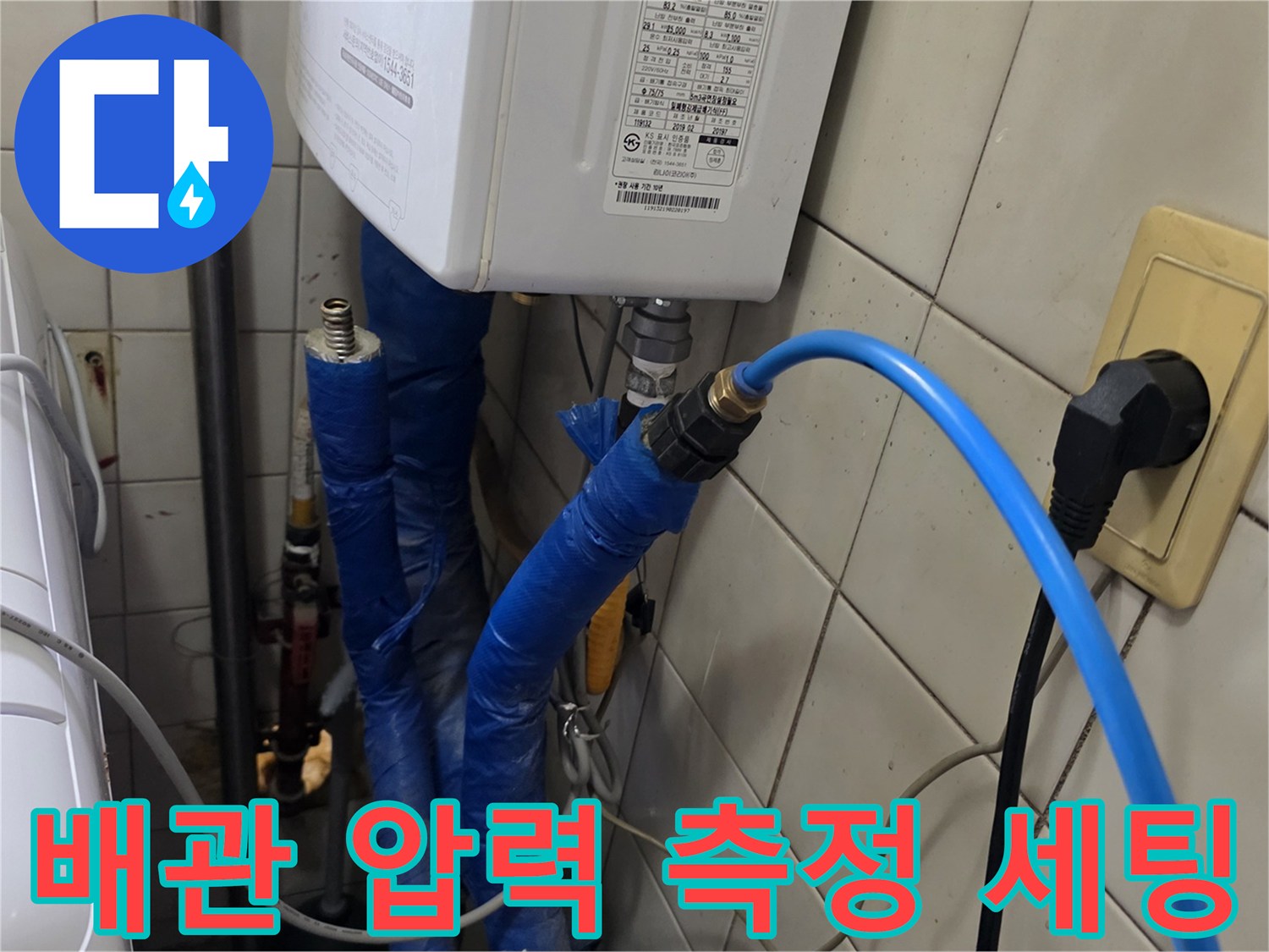 파란색 호스가 연결된 보일러실 하부 배관과 타일 벽면