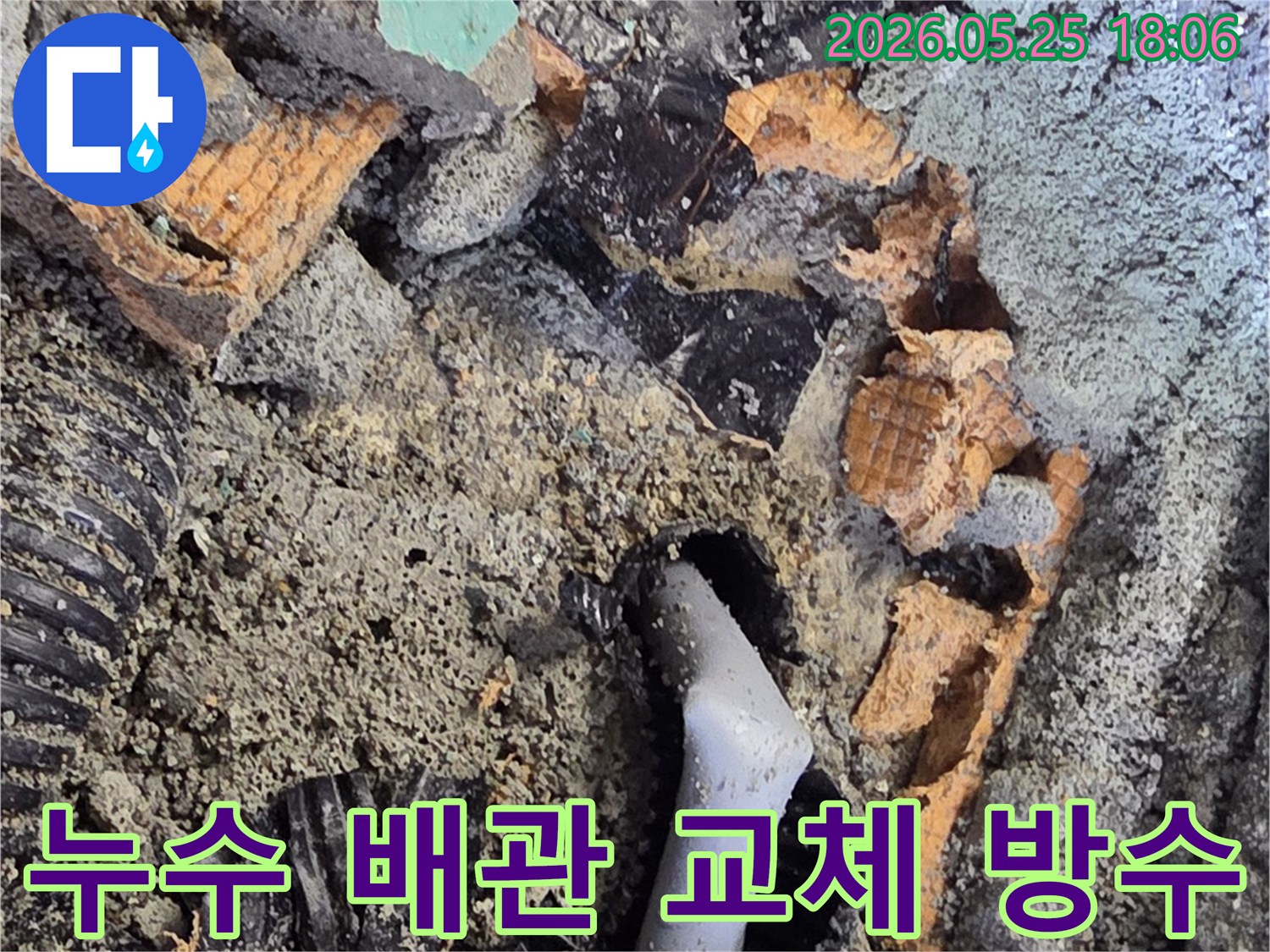 파쇄된 바닥 아래에서 드러난 젖은 배관과 주변의 흙-콘크리트 조각들은-누수 수리를 위한 배관 교체 작업을 보여줍니다.