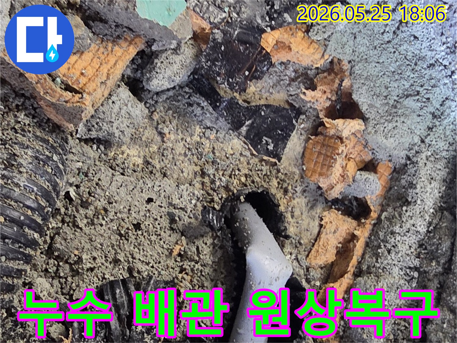 파쇄된 바닥 아래에서 드러난 젖은 배관과 주변의 흙-콘크리트 조각들은-누수 수리를 위한 배관 교체 작업을 보여줍니다.