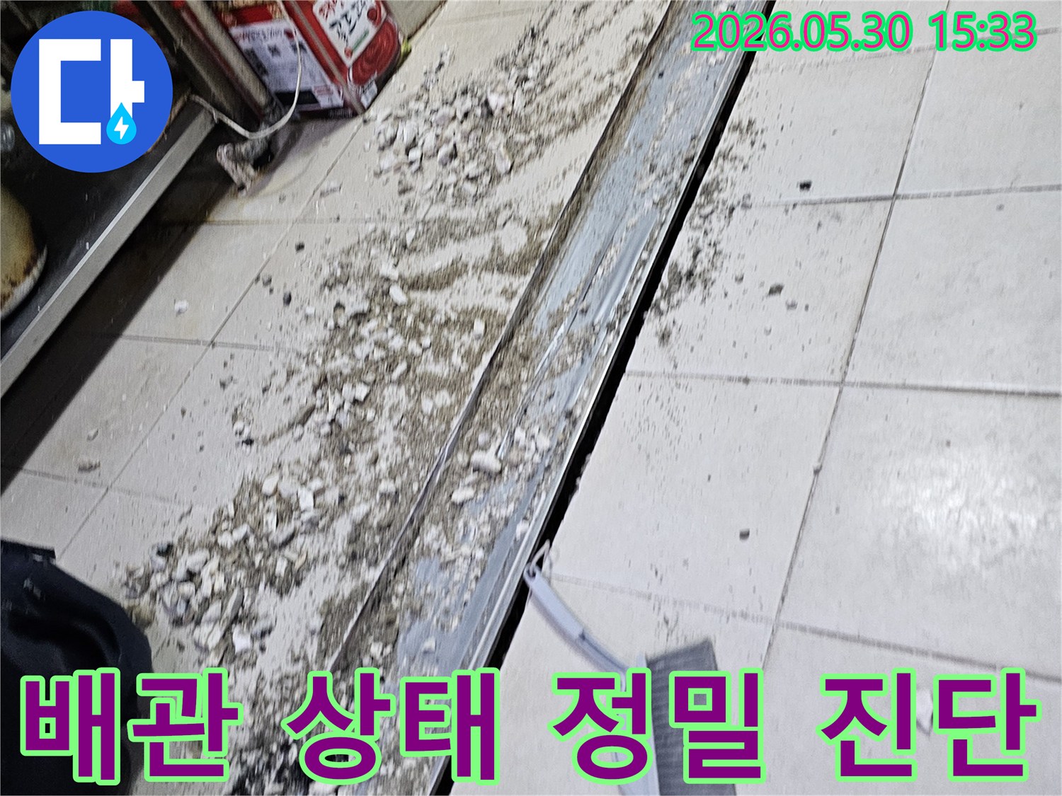 누수 공사 현장에서-바닥 타일 파쇄 후-발생한 잔해물과-청소 도구가-함께 보이는-작업 진행 모습입니다.