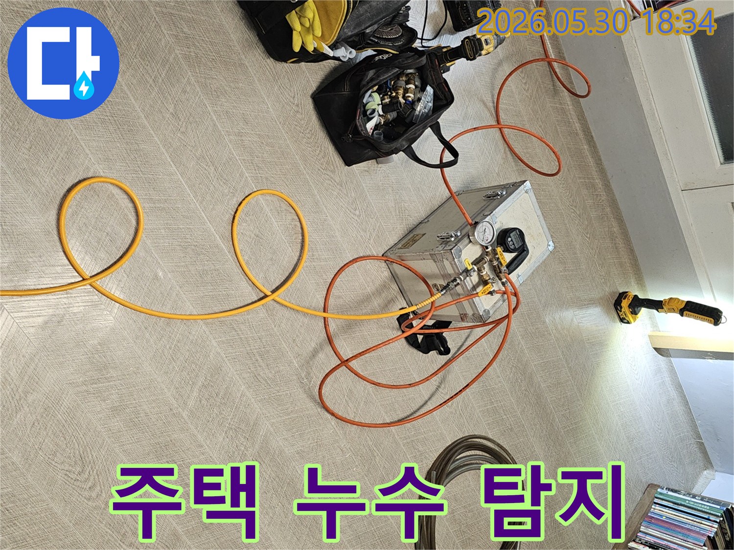 실내 바닥에 설치된 누수 탐지 장비와-다양한 연결 호스-그리고 작업 도구들이-누수 진단을 위해 준비된 장면입니다.