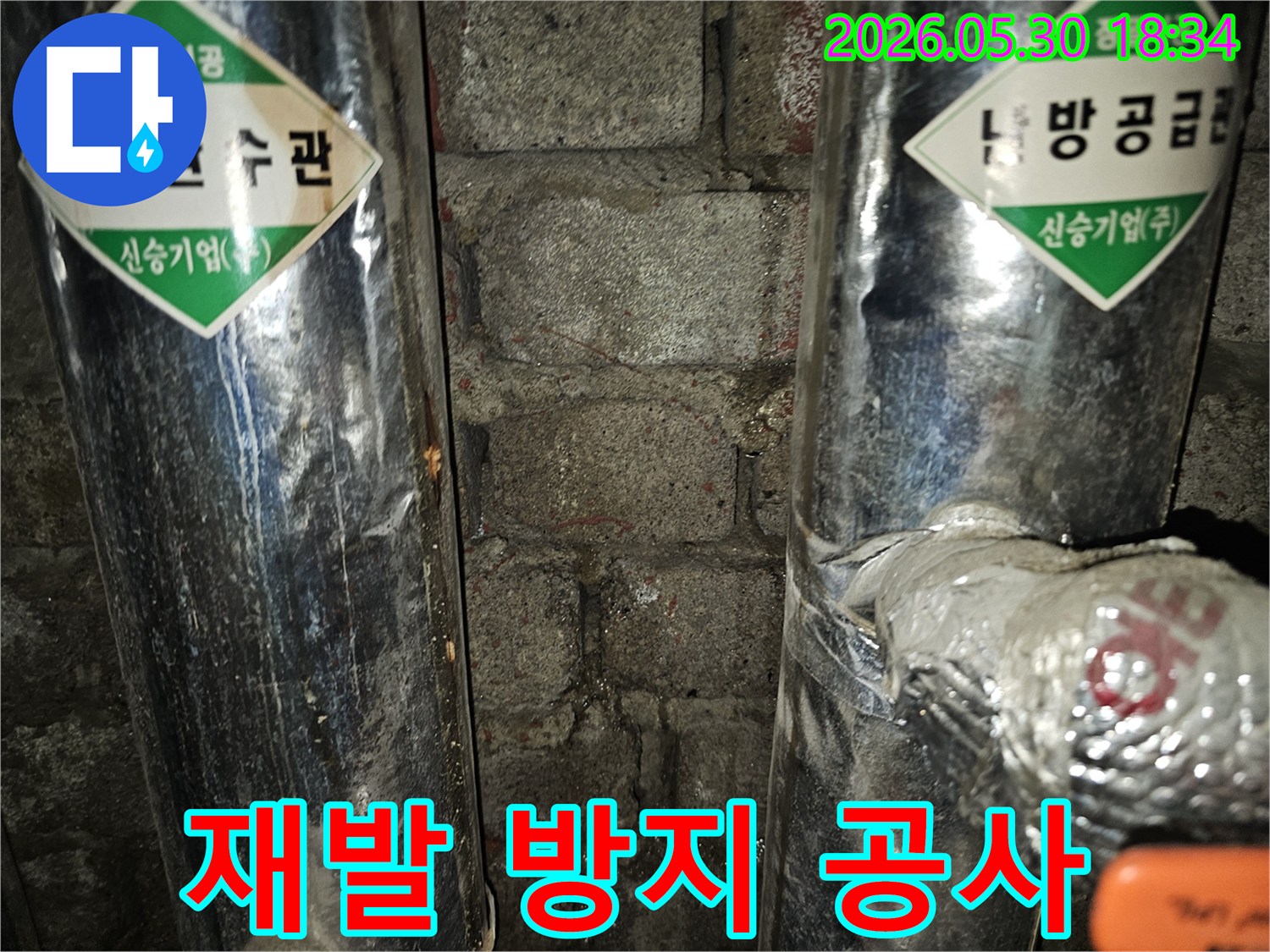 이 이미지는 오래된 벽돌 벽면과 환수관 사이에서-물이 새어 나와 벽을 적시고 있는-누수 현장의 재발 방지 공사 전 모습을 보여줍니다.