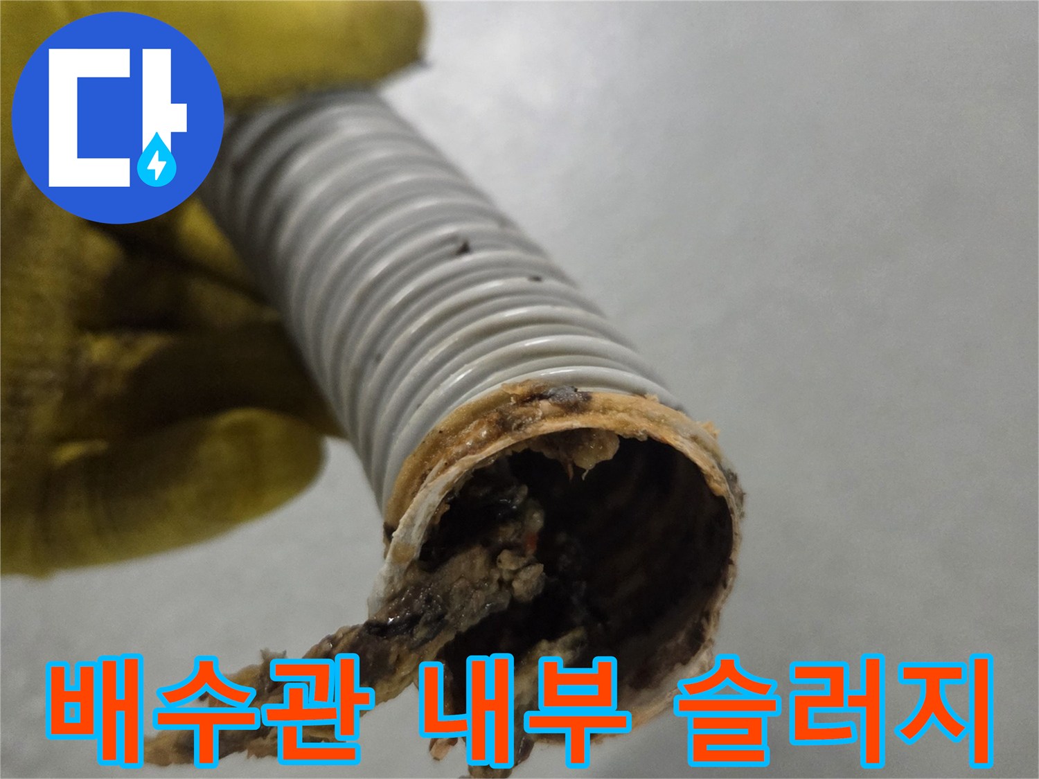 노란 장갑을 낀 작업자의 손이-오래된 슬러지로 막힌 배수관을 들고 있습니다.