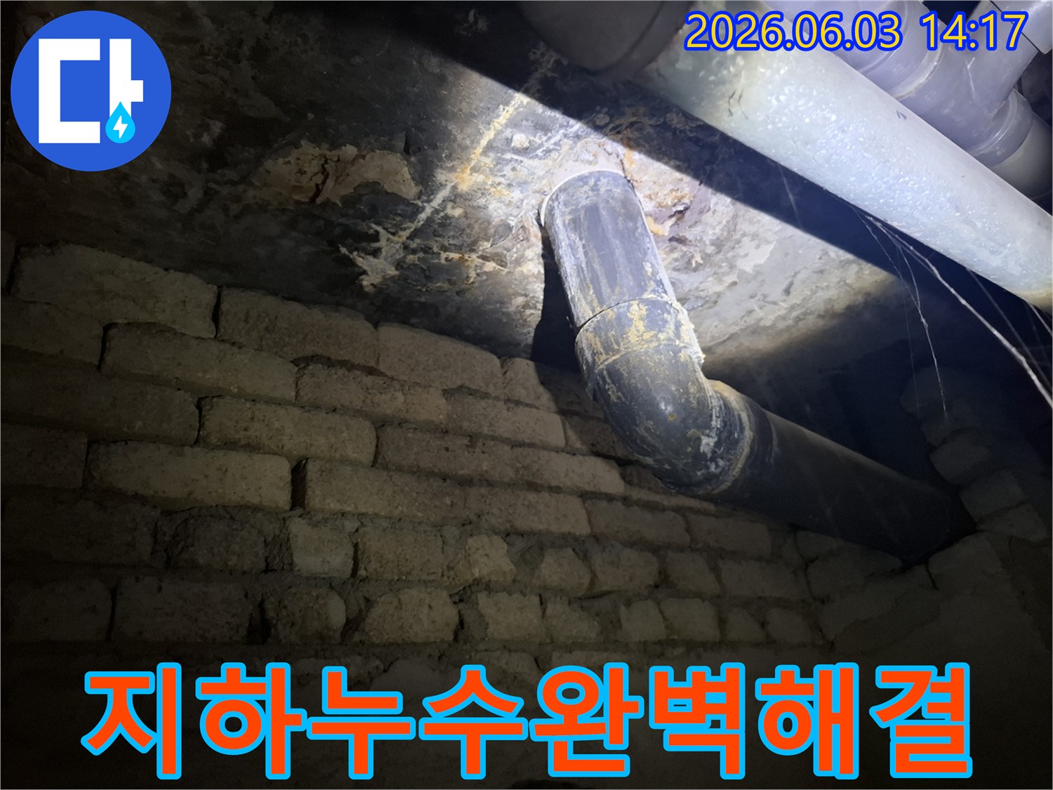 낡은 배관과-벽돌 벽이 있는-지하 공간에서-누수 발생 지점을-조명으로 비추며-세심하게 살펴보는 모습