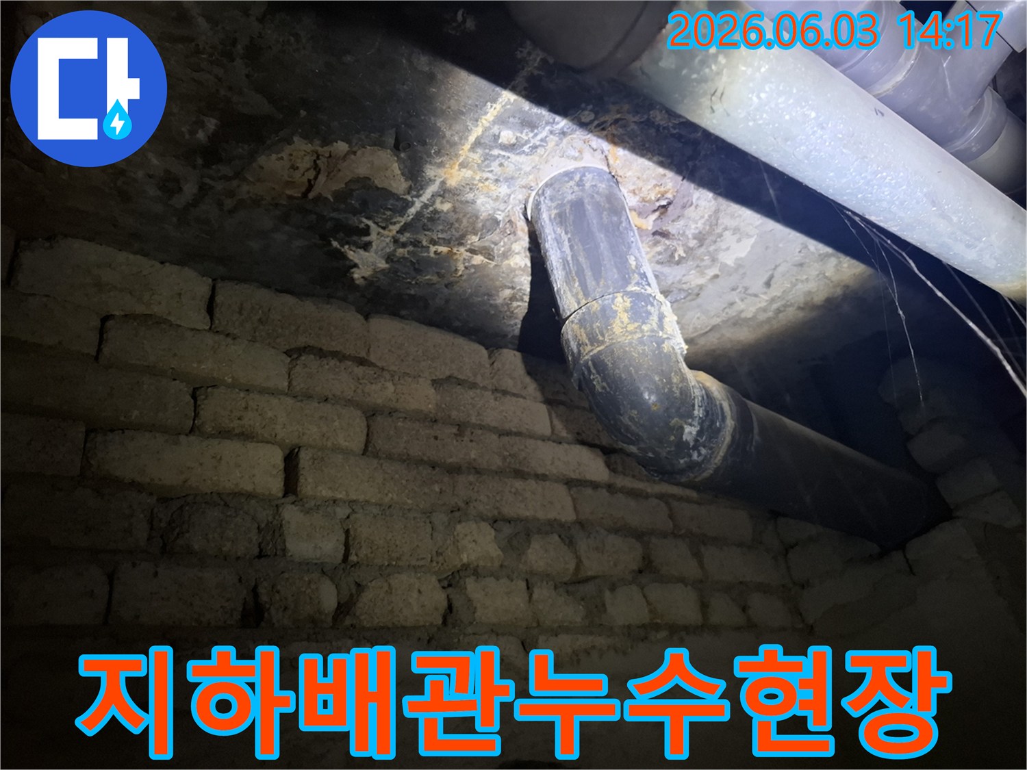 어두운 지하 공간에서-오래된 벽돌 벽과-배관 주변에 발생한-누수 흔적을-조명으로 비춰-정밀하게 확인하는 모습