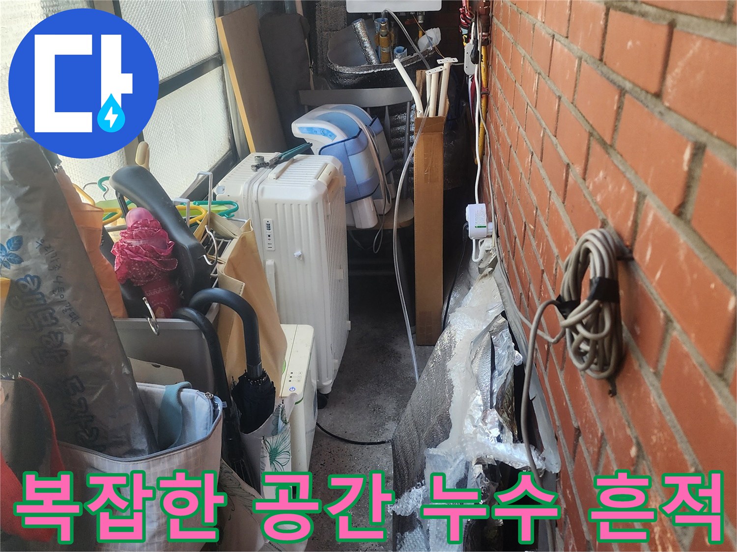 벽돌-벽-아래-복잡하게-얽힌-배관과-생활-용품들-사이에서-발견된-누수-흔적을-보여주는-사진