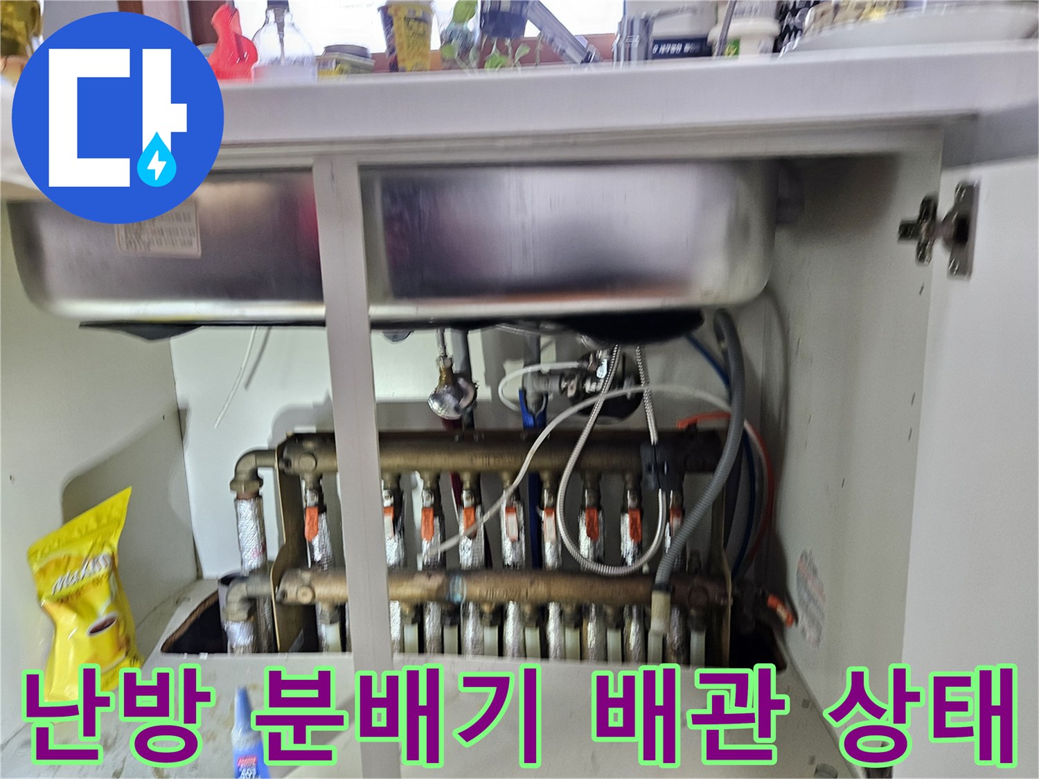 싱크대 하부장에 설치된 금속제 난방 분배기와 연결된 주름관 모습입니다.