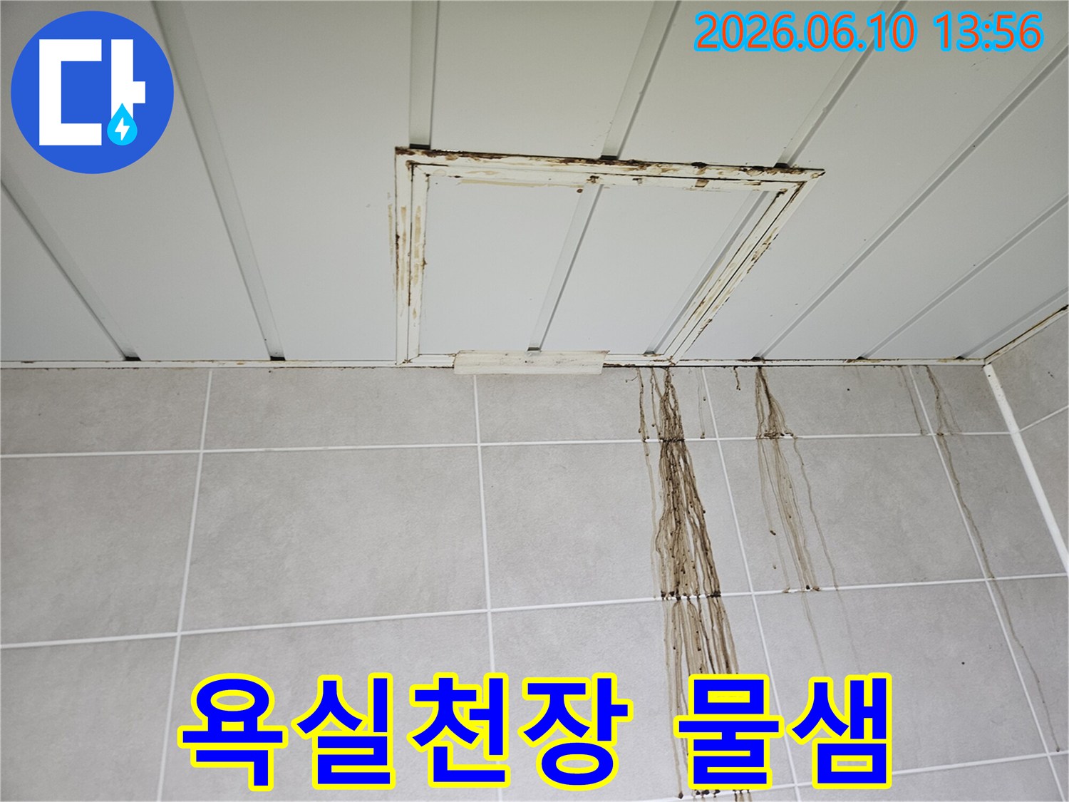 욕실 천장 점검구 주변에서 시작된 누수로-인해 타일 벽면이 오염된 모습을 보여줍니다.