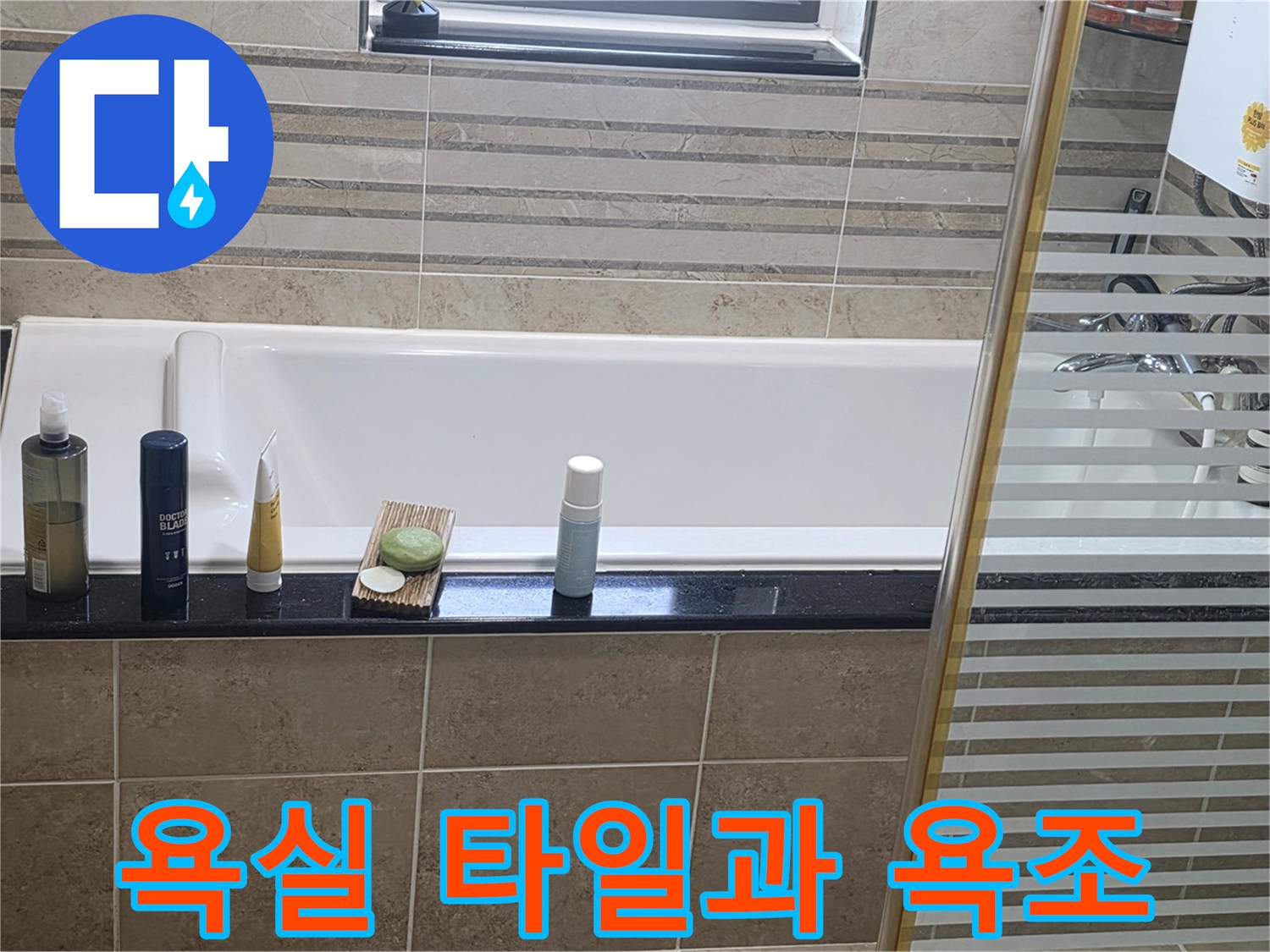 욕조 주변의 타일 마감재와 세면대 용품이 놓인 화장/실 내부 전경입니다.