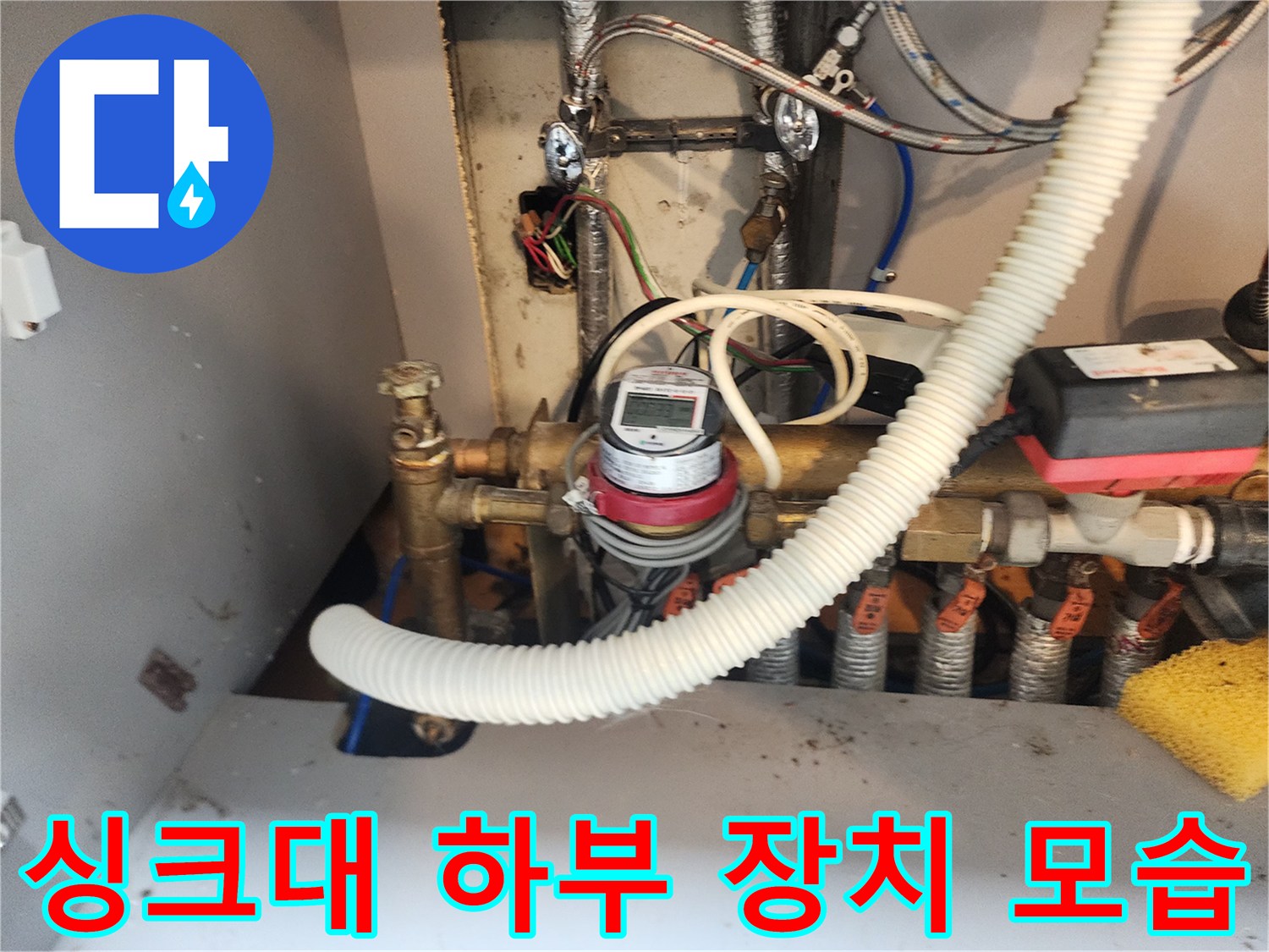주방 싱크대 아래쪽의 금속 밸브와 계량기 연결 부위입니다.