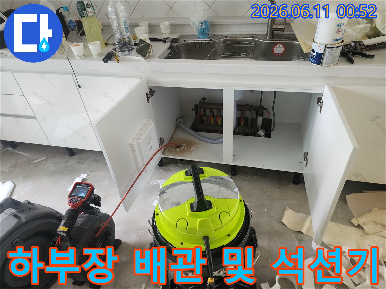 싱크대 하부장 내부의 노출된 배관과 노란색 석션 장비의 모습입니다.