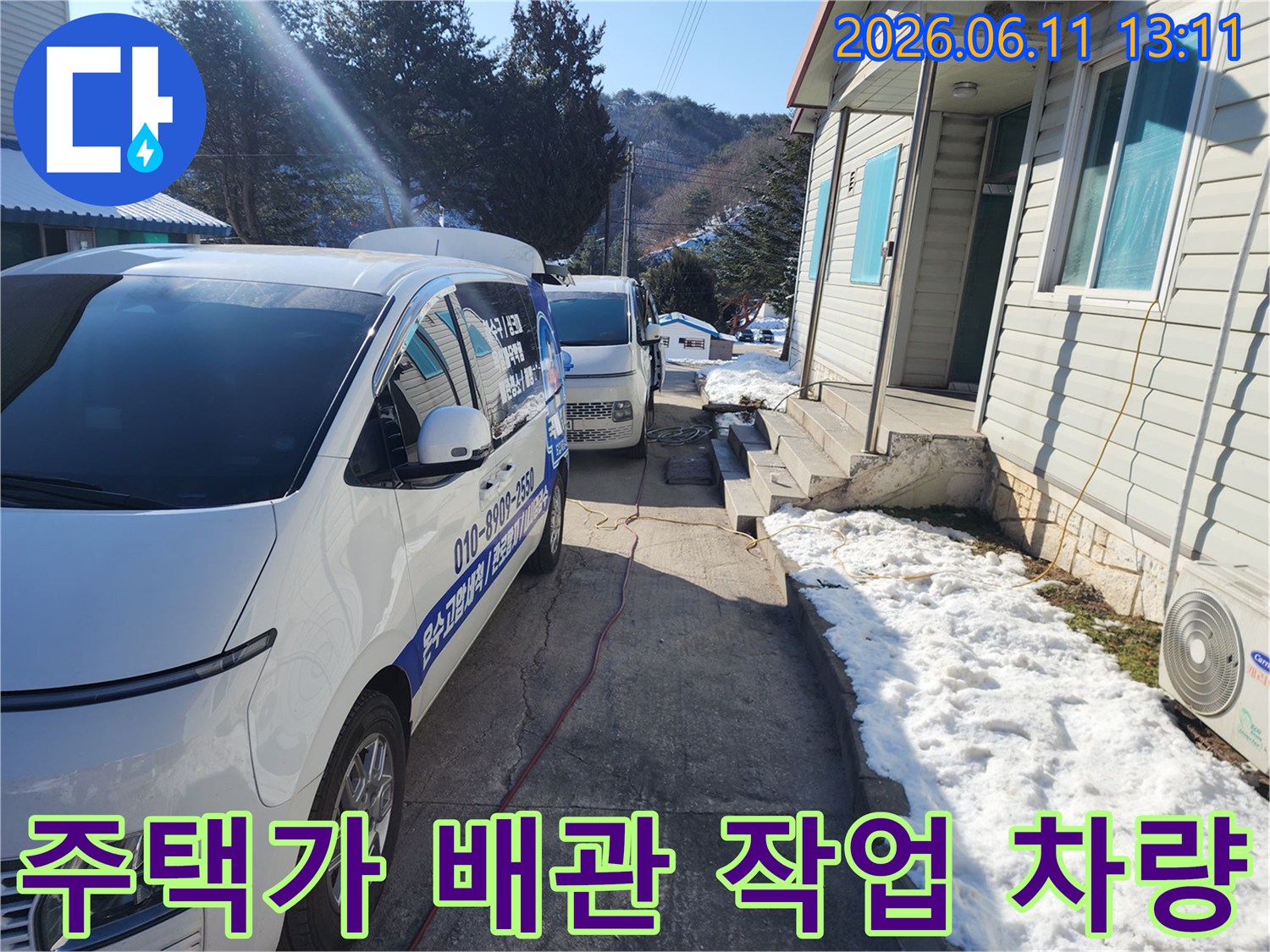 겨울철 눈 쌓인 주택 골목에 배치된 배관 작업 차량입니다.