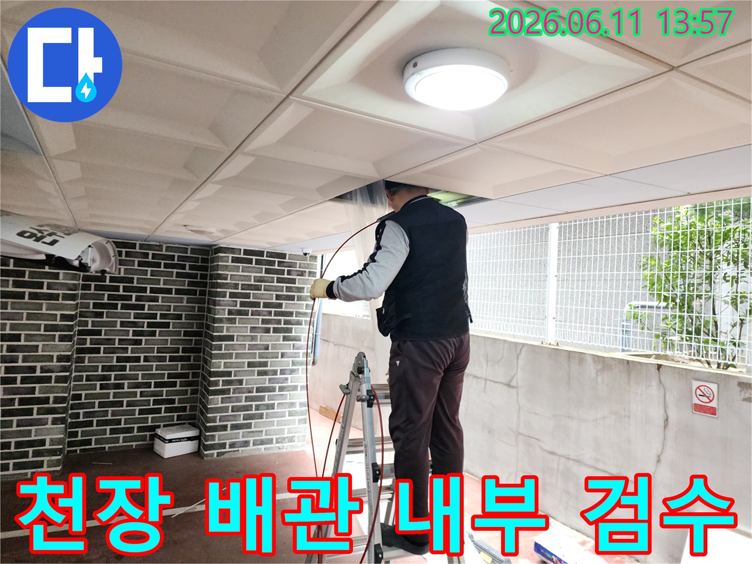 작업자가 사다리를 이용해-천장 패널 사이로 내시점 카메라를 넣어 배관 상태를 점검하는 장면입니다.