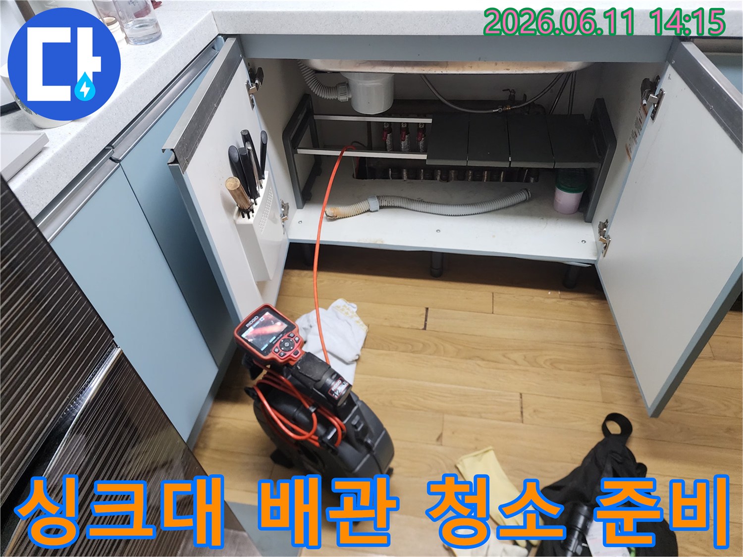 싱크대 하부장 내부의 배관과 작업용 장비들이 배치된 모습입니다.